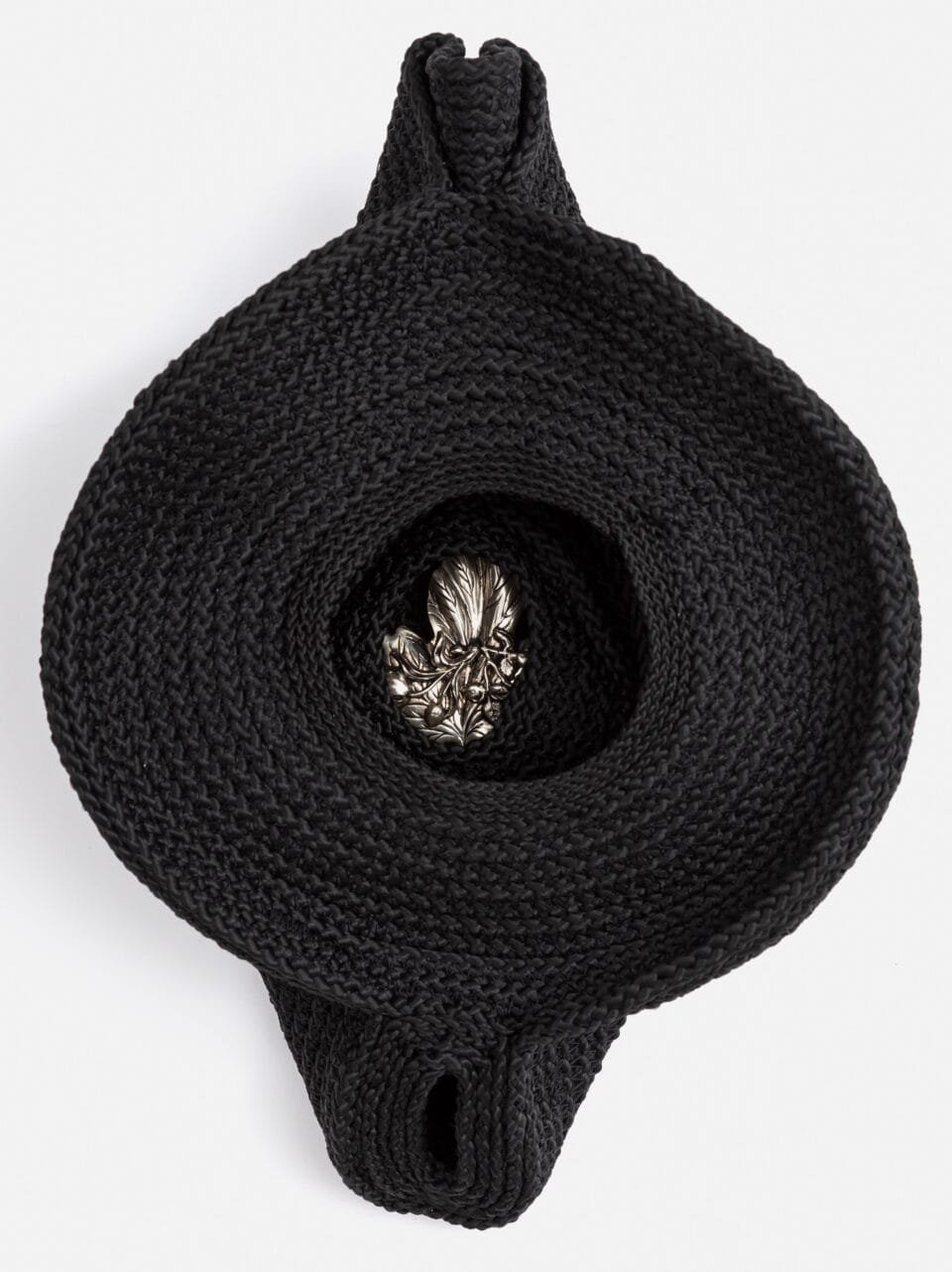 an artwork made from black cord, thread, and metal with a hole in the center with a shiny object in it