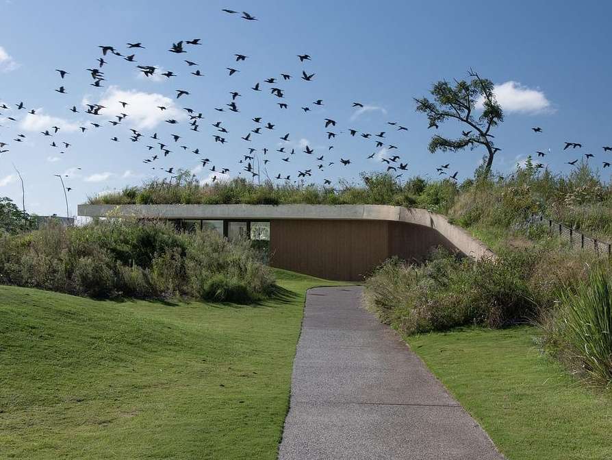 This concrete shell of this modern club house does double duty: it acts as both the building’s structure and surface, minimizing visual clutter and material use. The result is a continuous architectural form that feels quiet yet confident, merging seamlessly with its environment while inviting people to explore, gather, and linger.