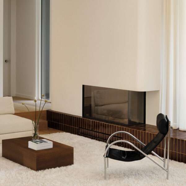 This sunken living room is both sculptural and serene. It creates an inviting, grounded space centered around a plush ivory rug and a terracotta tile platform. Rich in tone and laid with clean precision, the tile provides a grounding base for both the fireplace and the window wall.