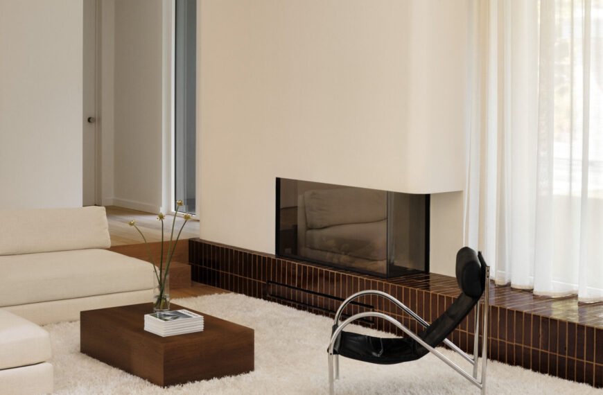 This sunken living room is both sculptural and serene. It creates an inviting, grounded space centered around a plush ivory rug and a terracotta tile platform. Rich in tone and laid with clean precision, the tile provides a grounding base for both the fireplace and the window wall.