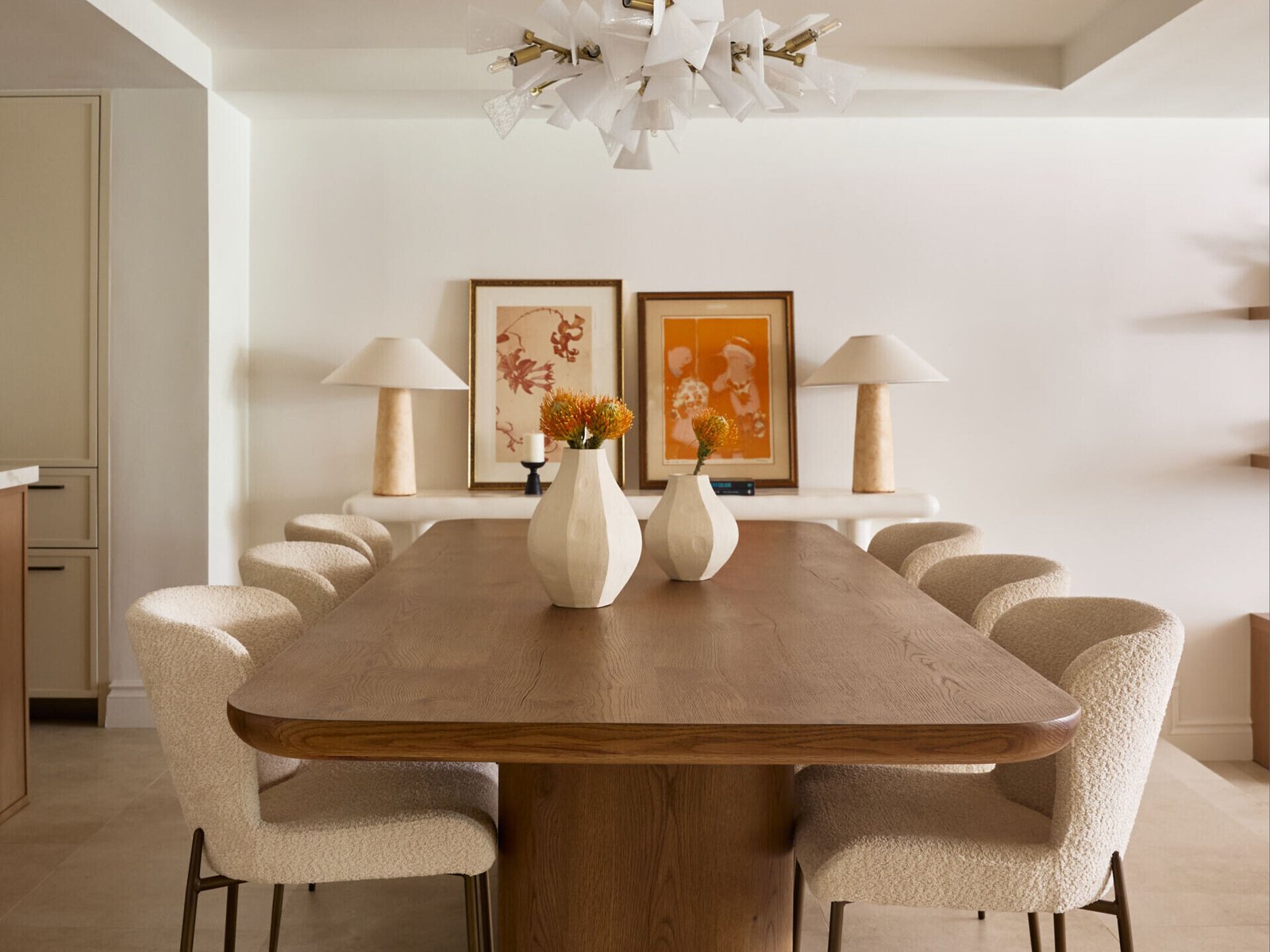 Sculptural but not stiff, this dining room is all about balance. A hefty, rounded-edge oak table grounds the space, while soft bouclé chairs bring texture and tactility. Above, a dramatic chandelier with layered white shards adds an artful contrast to the natural palette.
