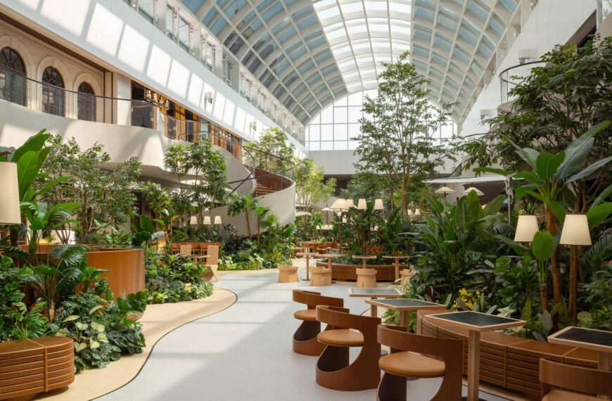 A transparent arched skylight transforms this indoor public garden space with natural light. Steel curves echo leaf veins while shifting sun patterns on the floor mimic moss growing in a greenhouse. A calming, nature-inspired design moment.