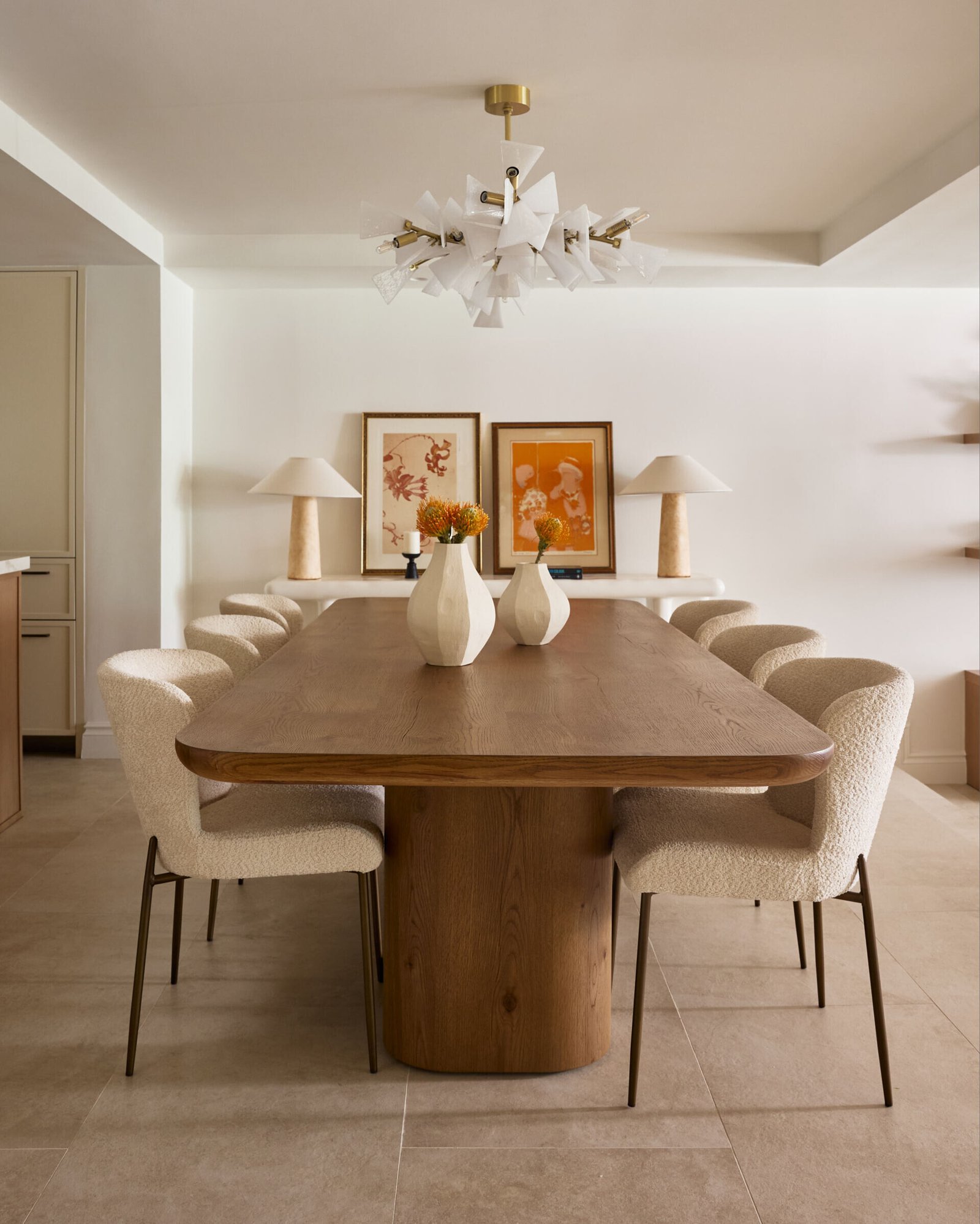 Sculptural but not stiff, this dining room is all about balance. A hefty, rounded-edge oak table grounds the space, while soft bouclé chairs bring texture and tactility. Above, a dramatic chandelier with layered white shards adds an artful contrast to the natural palette. 