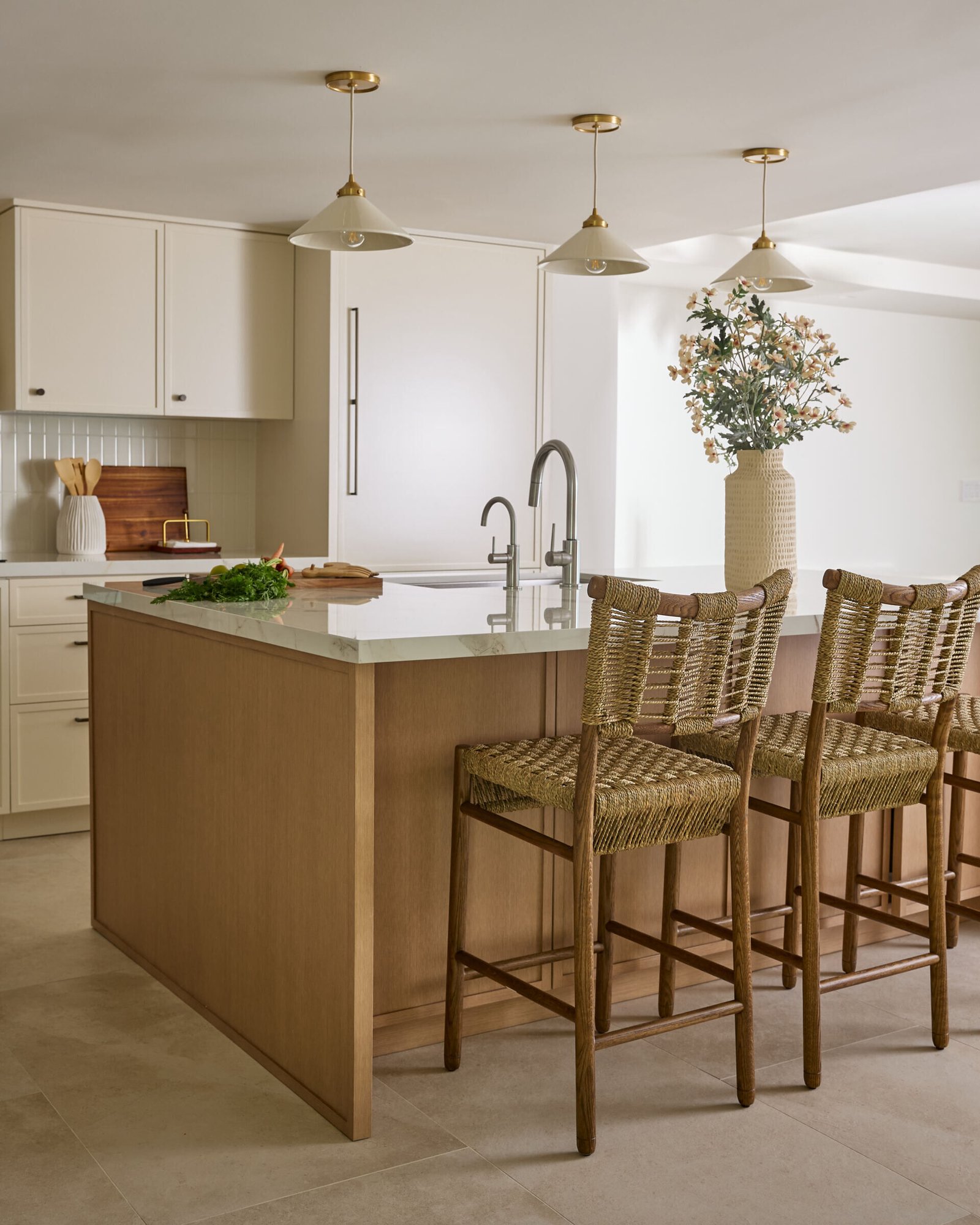This updated kitchen manages to be both practical and picturesque. Creamy cabinetry is elevated by vertically stacked zellige tiles and dark bronze hardware, while a custom oak island topped with Dekton stone brings warmth and functionality. Brass and ceramic pendant lights overhead lend a vintage glow, and the whole space feels calm, considered, and deeply livable.