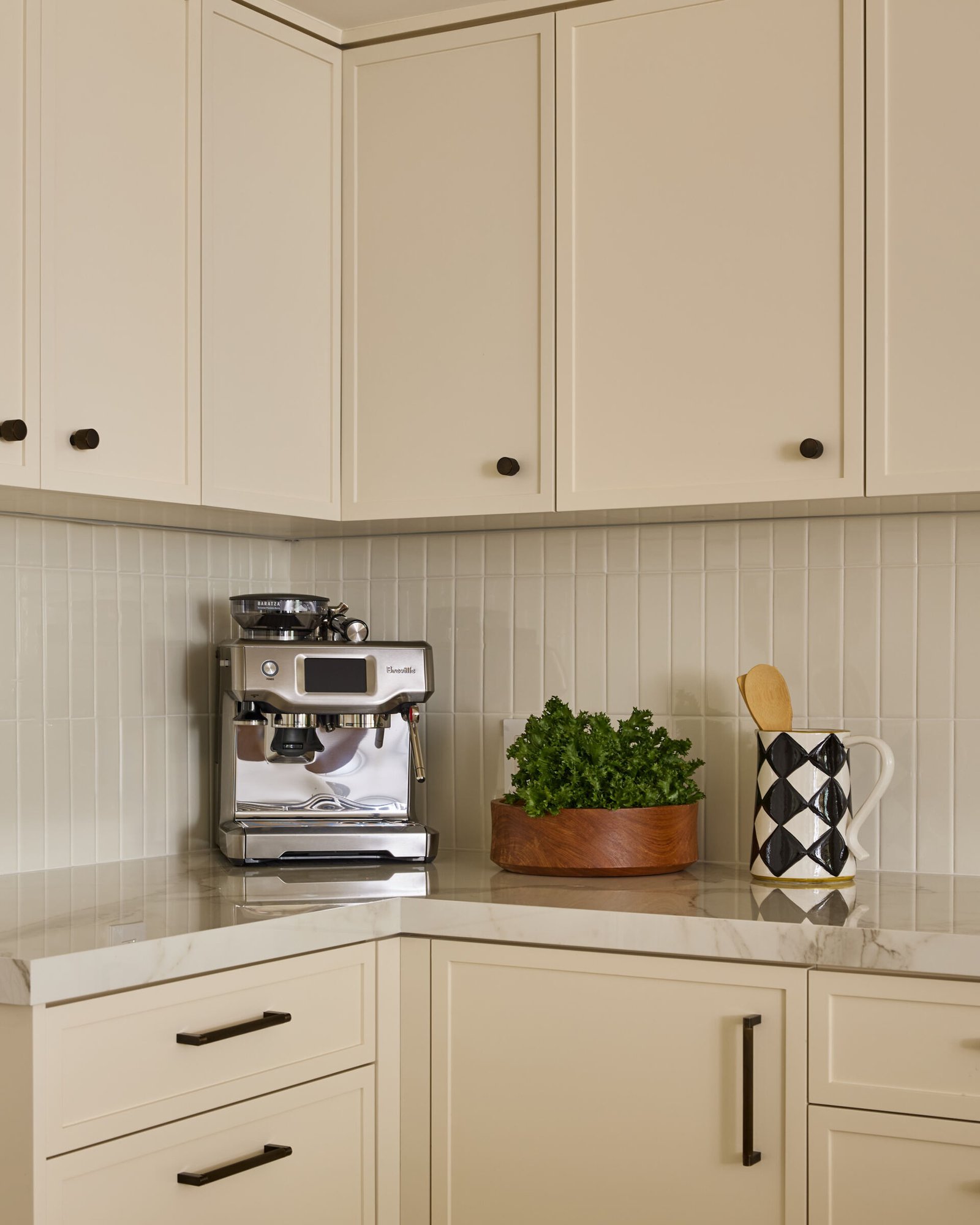 This updated kitchen manages to be both practical and picturesque. Creamy cabinetry is elevated by vertically stacked zellige tiles and dark bronze hardware, while a custom oak island topped with Dekton stone brings warmth and functionality. Brass and ceramic pendant lights overhead lend a vintage glow, and the whole space feels calm, considered, and deeply livable.