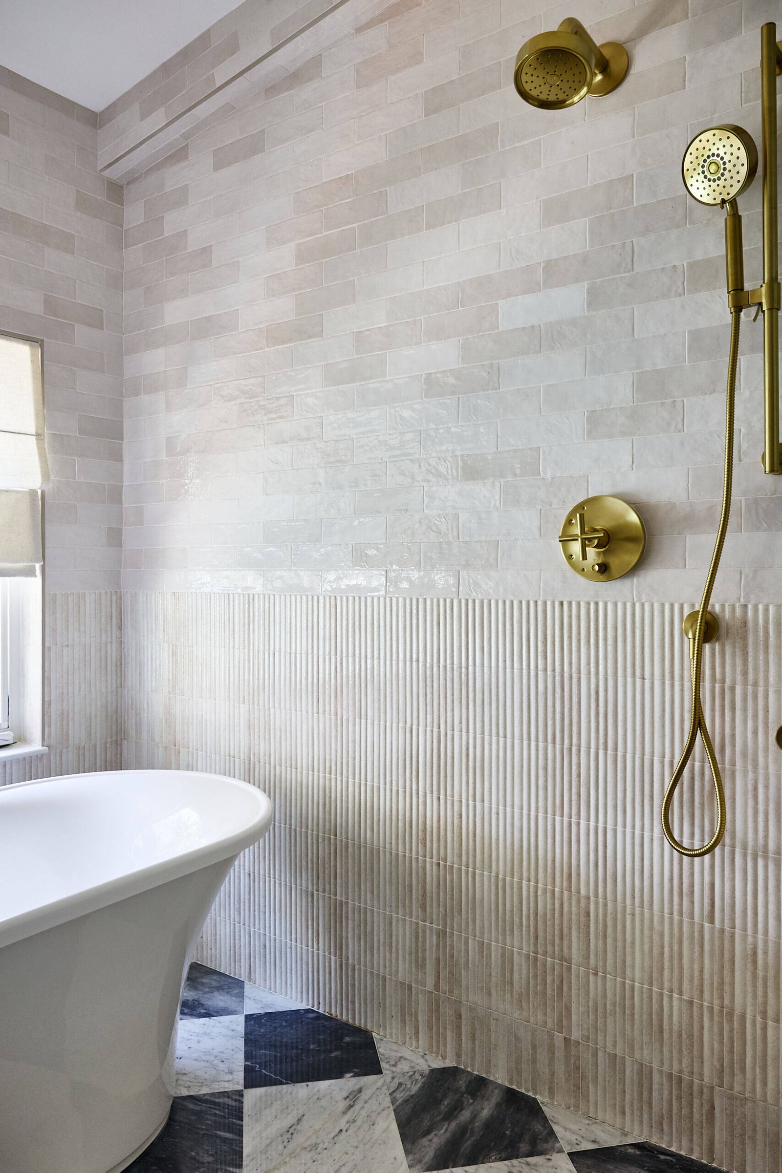 In this primary bath, quiet indulgence is the theme. The checkerboard marble floor adds a timeless graphic punch, offset by creamy wall tiles that bring in softness. A freestanding tub basks in sunlight and lake views, while the custom oak vanity topped with honed marble strikes a clean yet classic tone. Brass fixtures, gold-rimmed mirrors, and alabaster sconces round out the palette in glowing harmony.