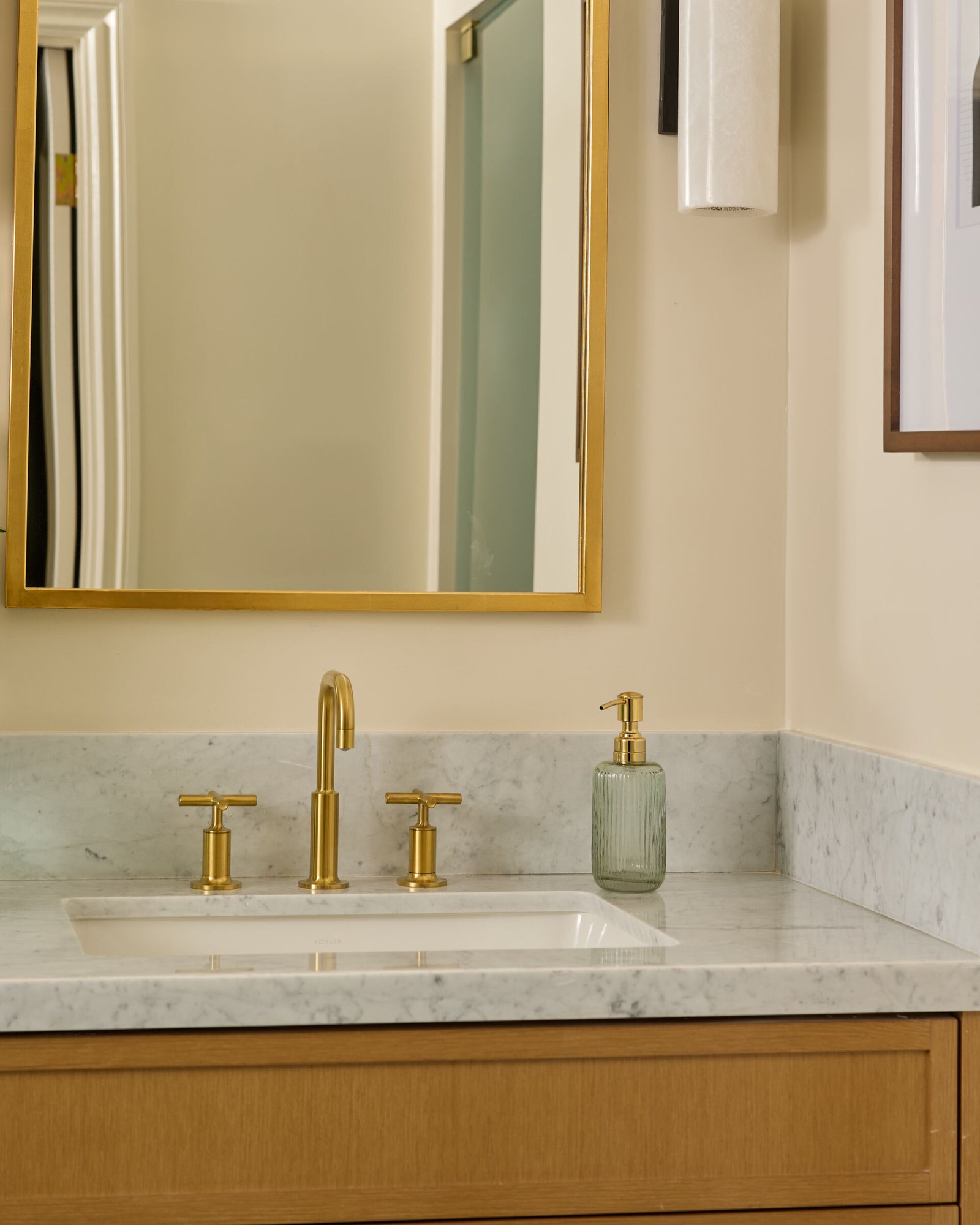 In this primary bath, quiet indulgence is the theme. The checkerboard marble floor adds a timeless graphic punch, offset by creamy wall tiles that bring in softness. A freestanding tub basks in sunlight and lake views, while the custom oak vanity topped with honed marble strikes a clean yet classic tone. Brass fixtures, gold-rimmed mirrors, and alabaster sconces round out the palette in glowing harmony.