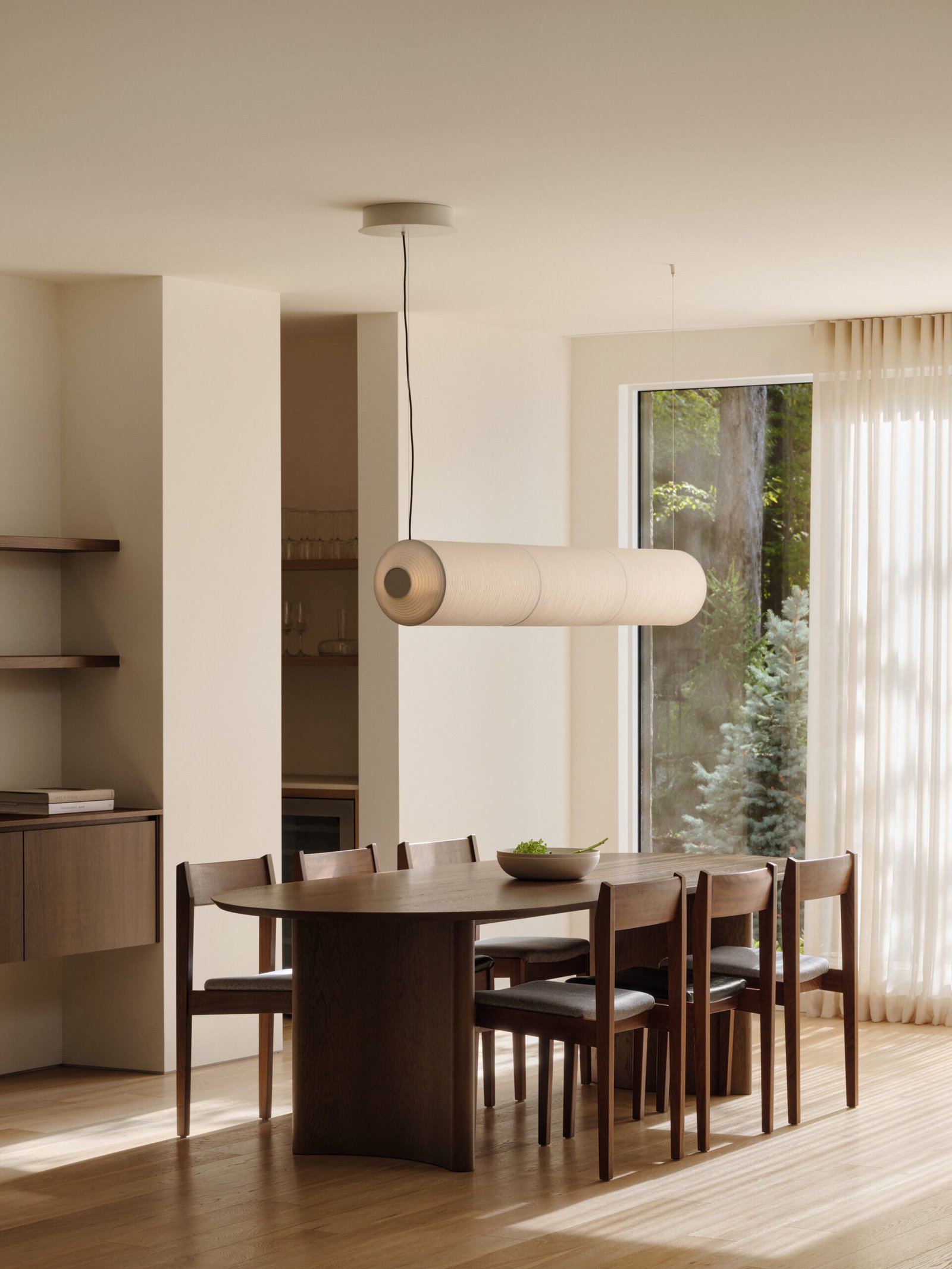 Just beyond the living room, the dining space explores balance through contrast. A dark wood table plays against a light oak floor, continuing the project’s recurring dialogue between rich materials and natural softness. Curved lines, seen in walls and furniture, create continuity and quiet movement.
