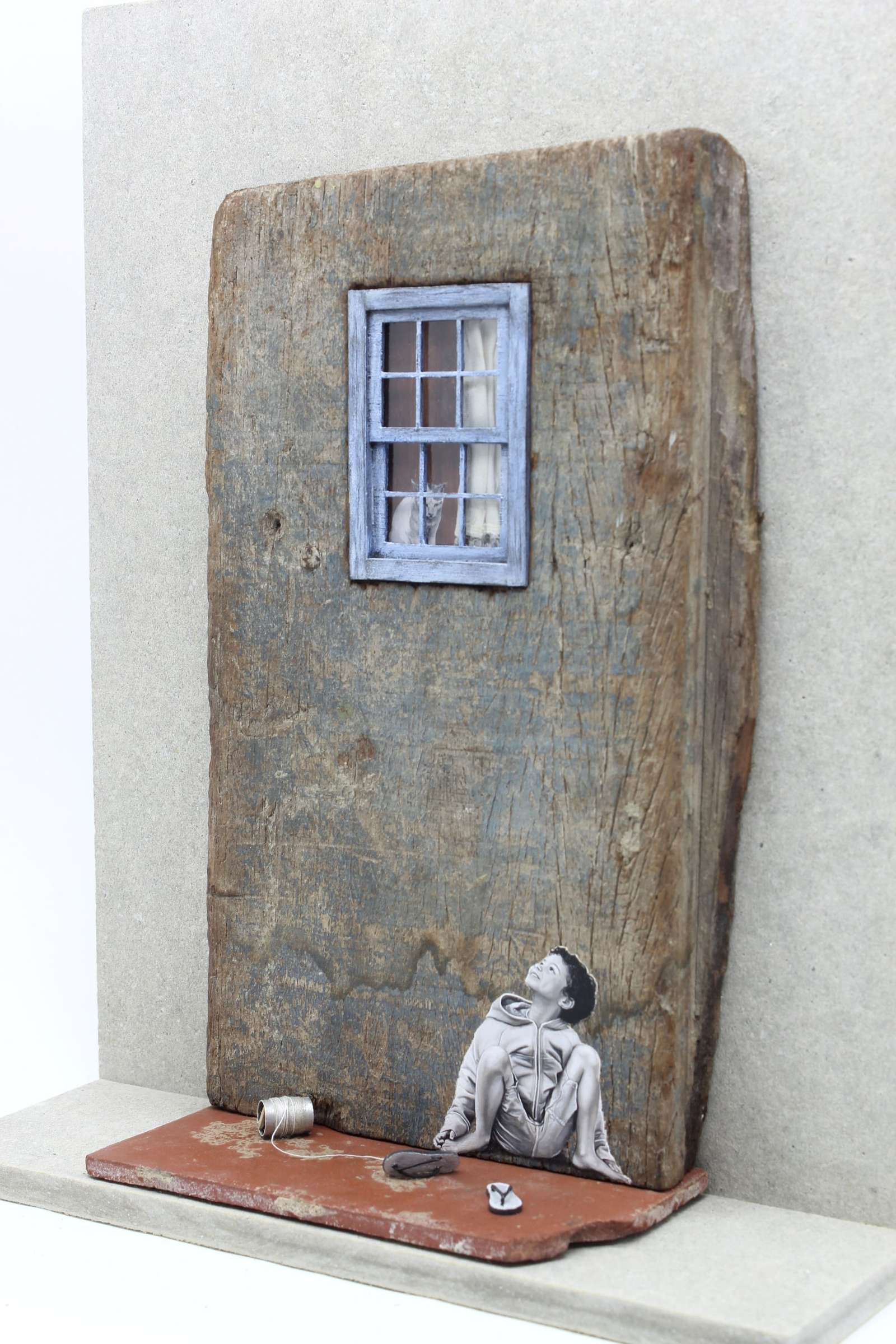 a seated child with sculptural flip flips and rope in front of him is painted on a fragment of wood with a window above