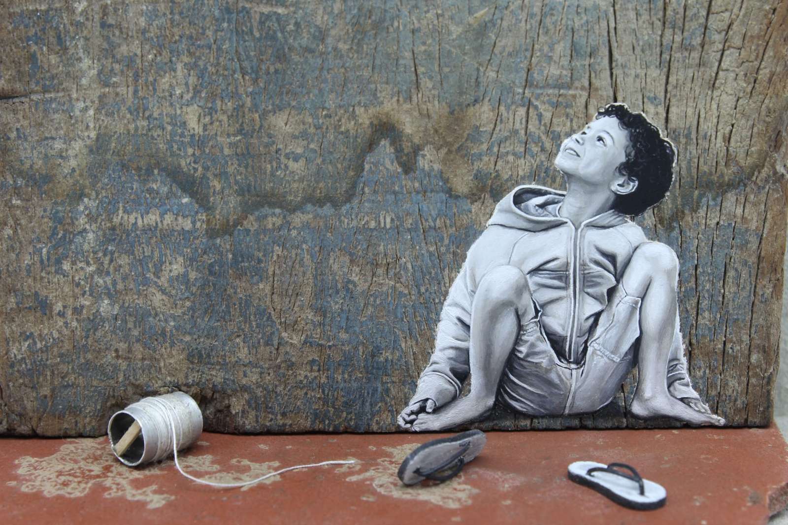 a detail of a seated child with sculptural flip flips and rope in front of him