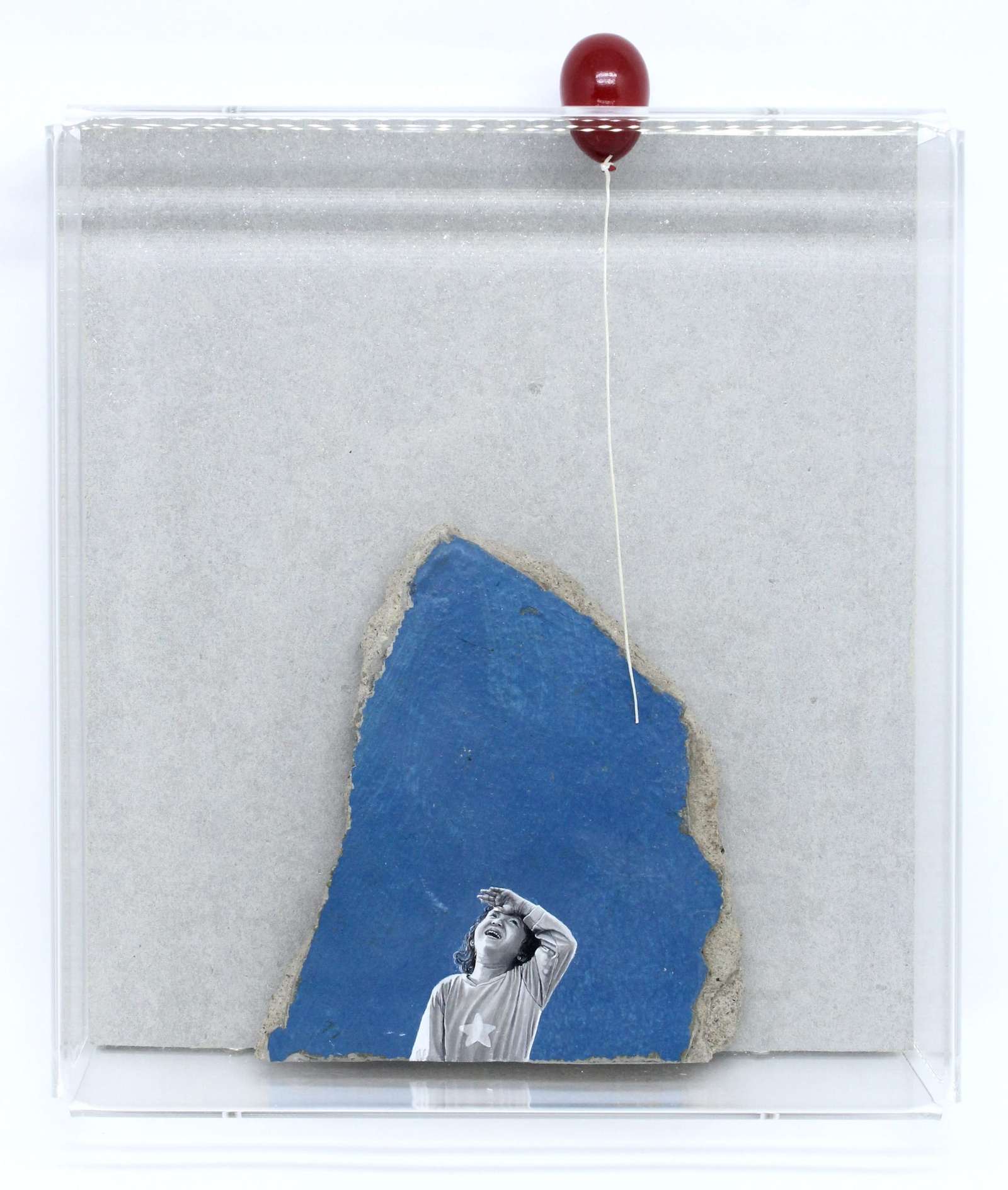 a child painted on a fragment of blue concrete looks up at a sculptural red balloon that peeks out of the frame