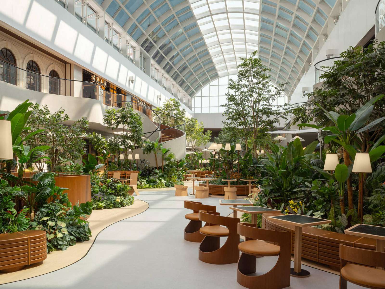 A transparent arched skylight transforms this indoor public garden space with natural light. Steel curves echo leaf veins while shifting sun patterns on the floor mimic moss growing in a greenhouse. A calming, nature-inspired design moment.