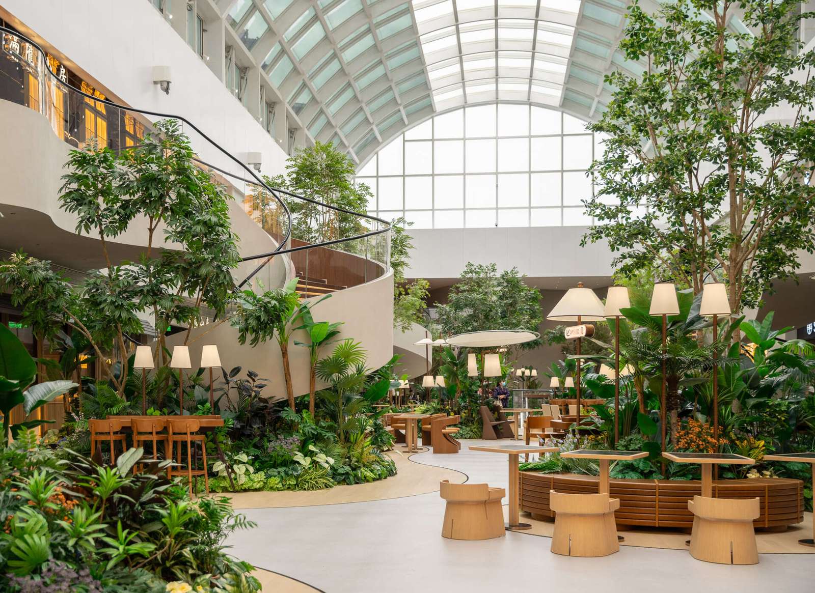 A transparent arched skylight transforms this indoor public garden space with natural light. Steel curves echo leaf veins while shifting sun patterns on the floor mimic moss growing in a greenhouse. A calming, nature-inspired design moment.