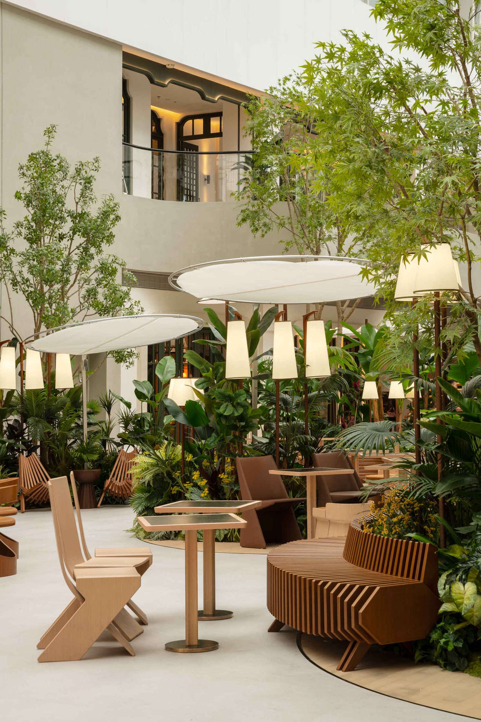 In this public plaza, long benches curve around clusters of greenery while sculptural chairs create relaxed, flexible seating. This dining space flows into a shared public garden, dissolving the line between restaurant and rest stop.