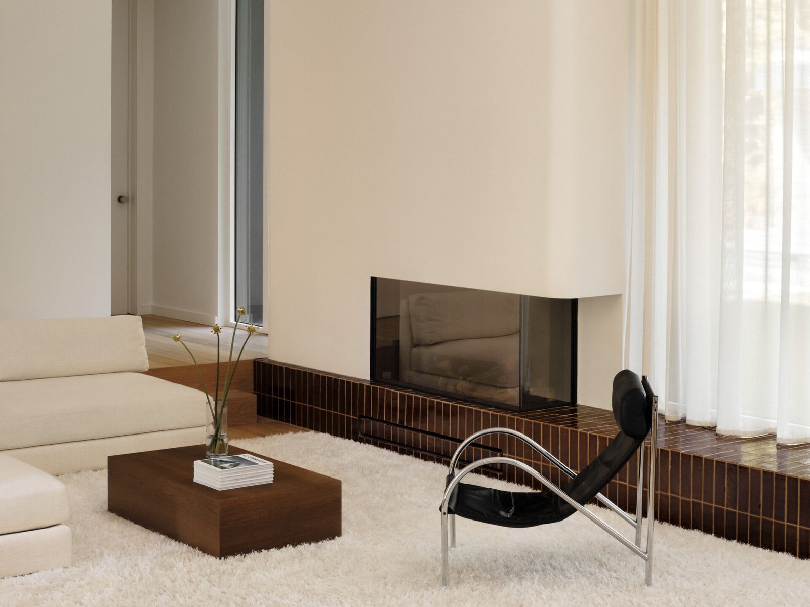 This sunken living room is both sculptural and serene. It creates an inviting, grounded space centered around a plush ivory rug and a terracotta tile platform. Rich in tone and laid with clean precision, the tile provides a grounding base for both the fireplace and the window wall.