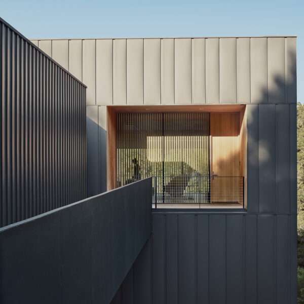 The exterior of this modern home is wrapped in vertical steel panels designed to weather, while deep wood-lined recesses frame curated views and allow light to shift throughout the day.