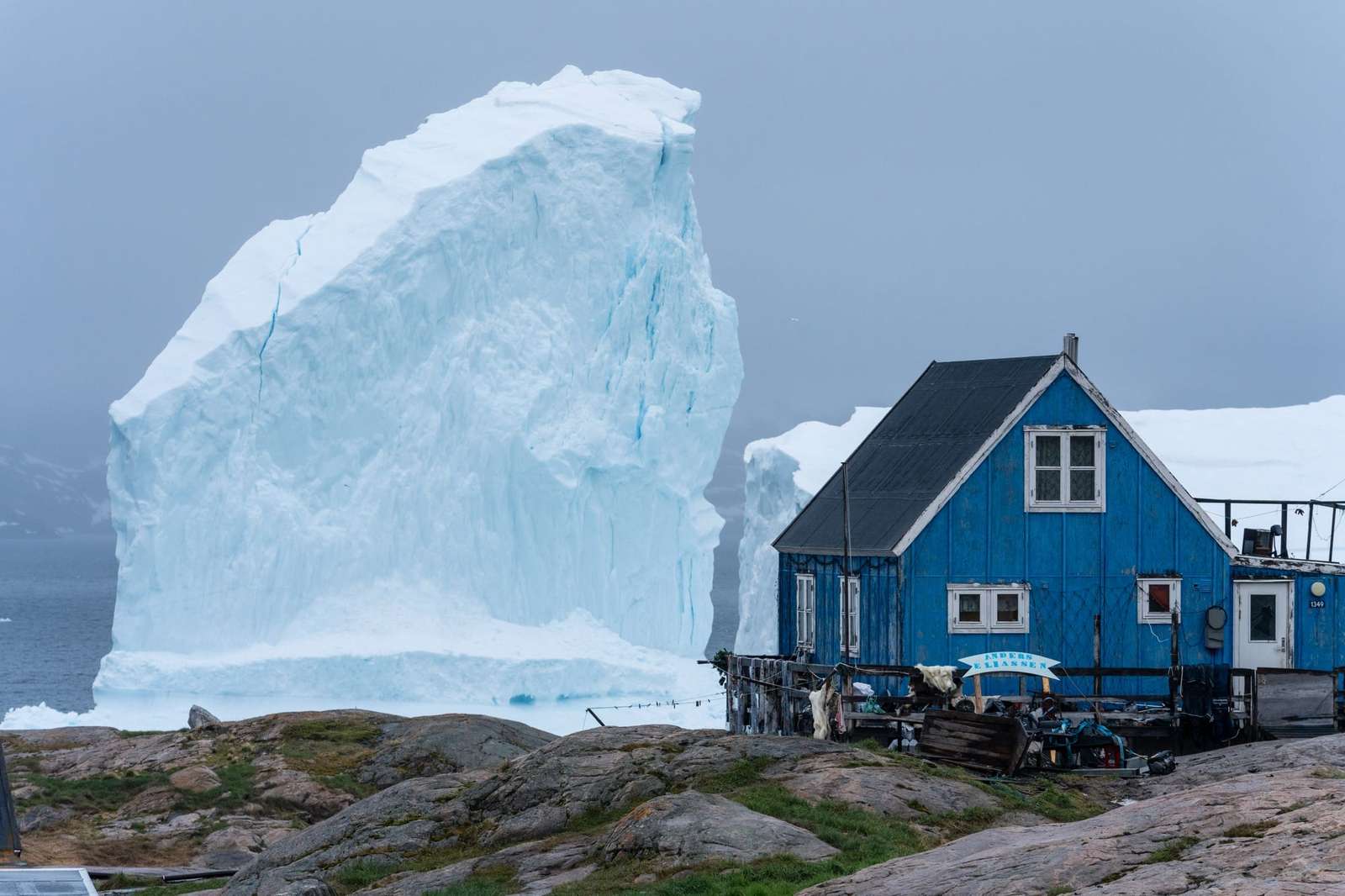 a small house in Greenland with a giant iceberg in the background