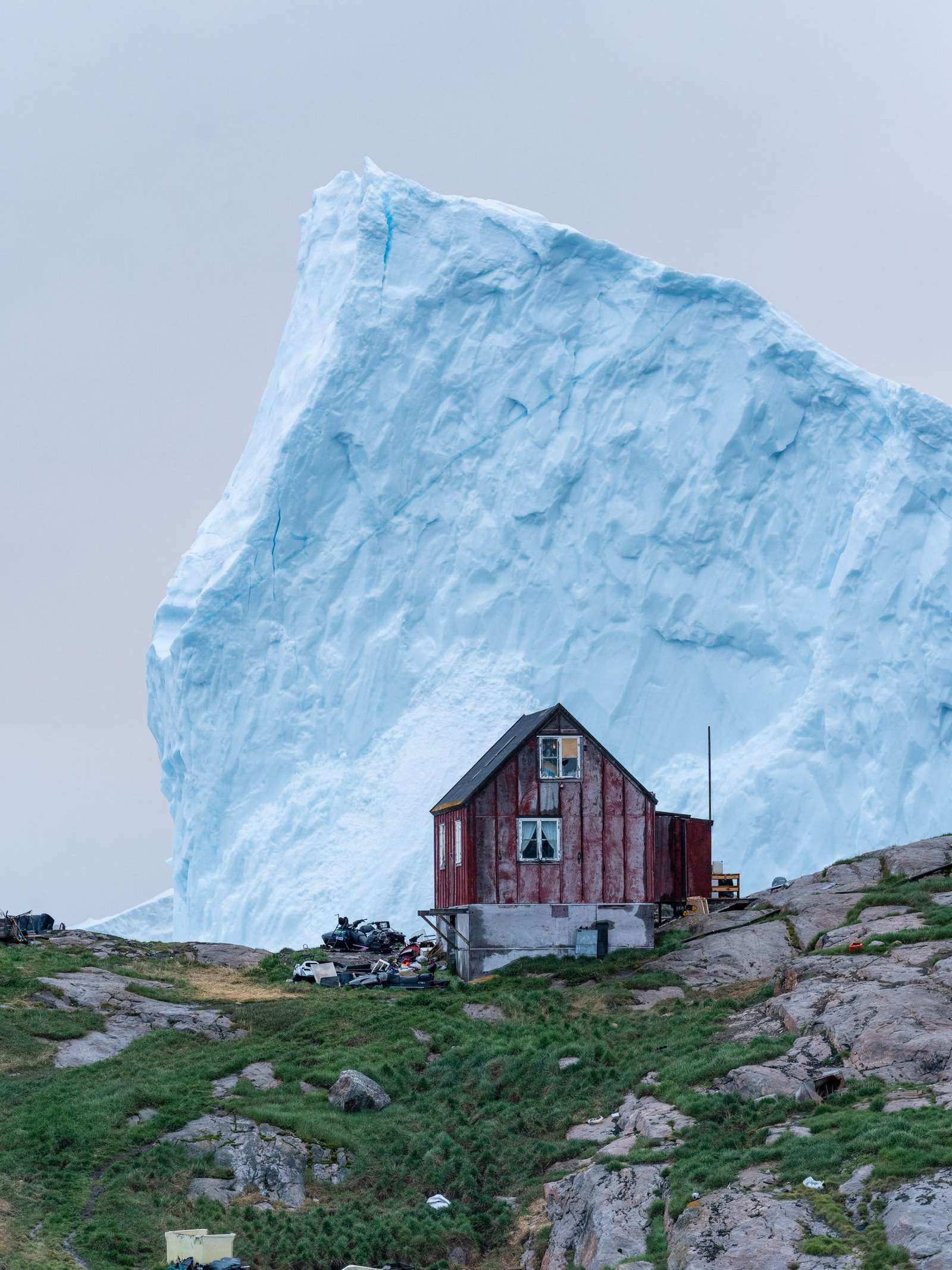a small house in Greenland with a giant iceberg in the background