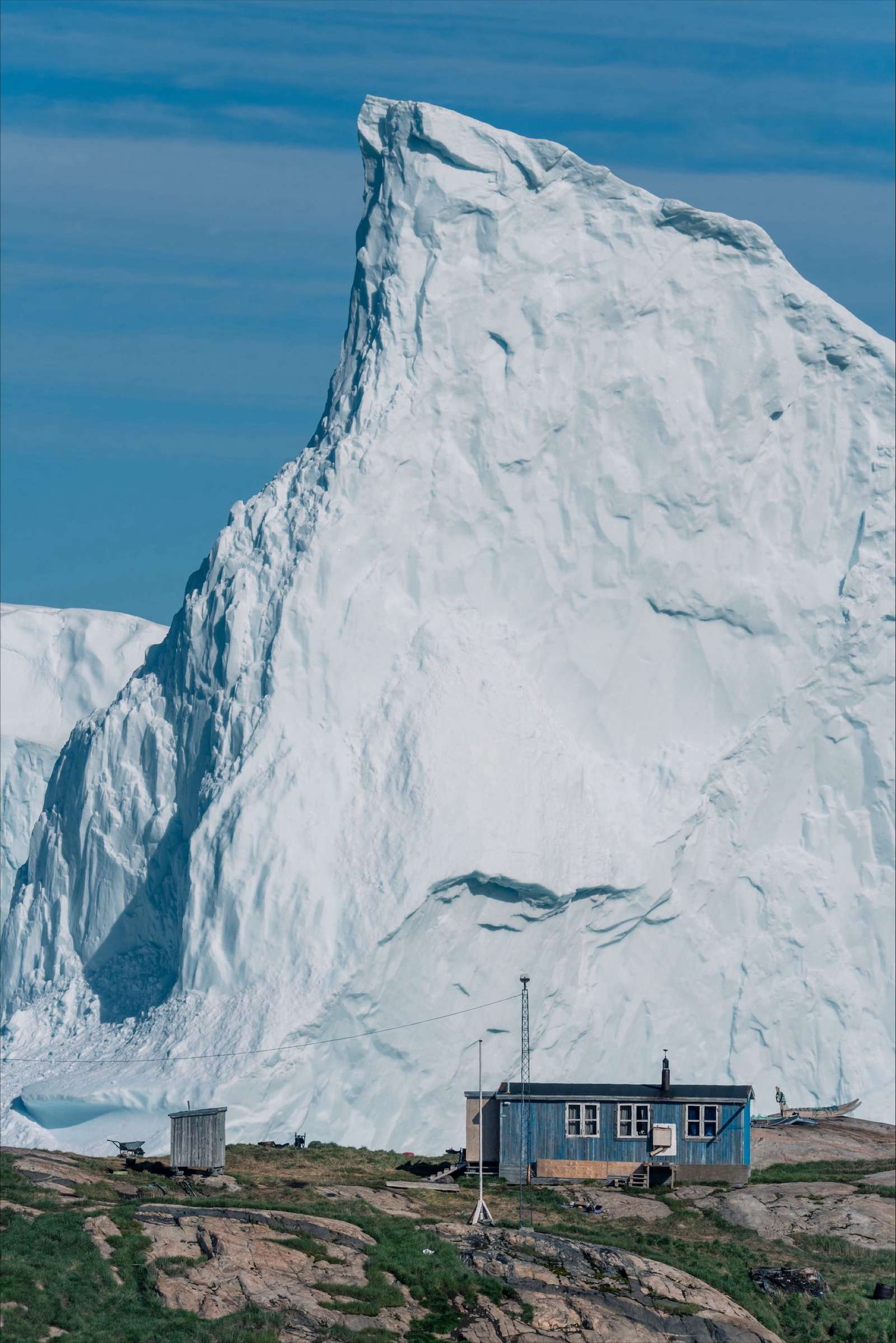 a small house in Greenland with a giant iceberg in the background