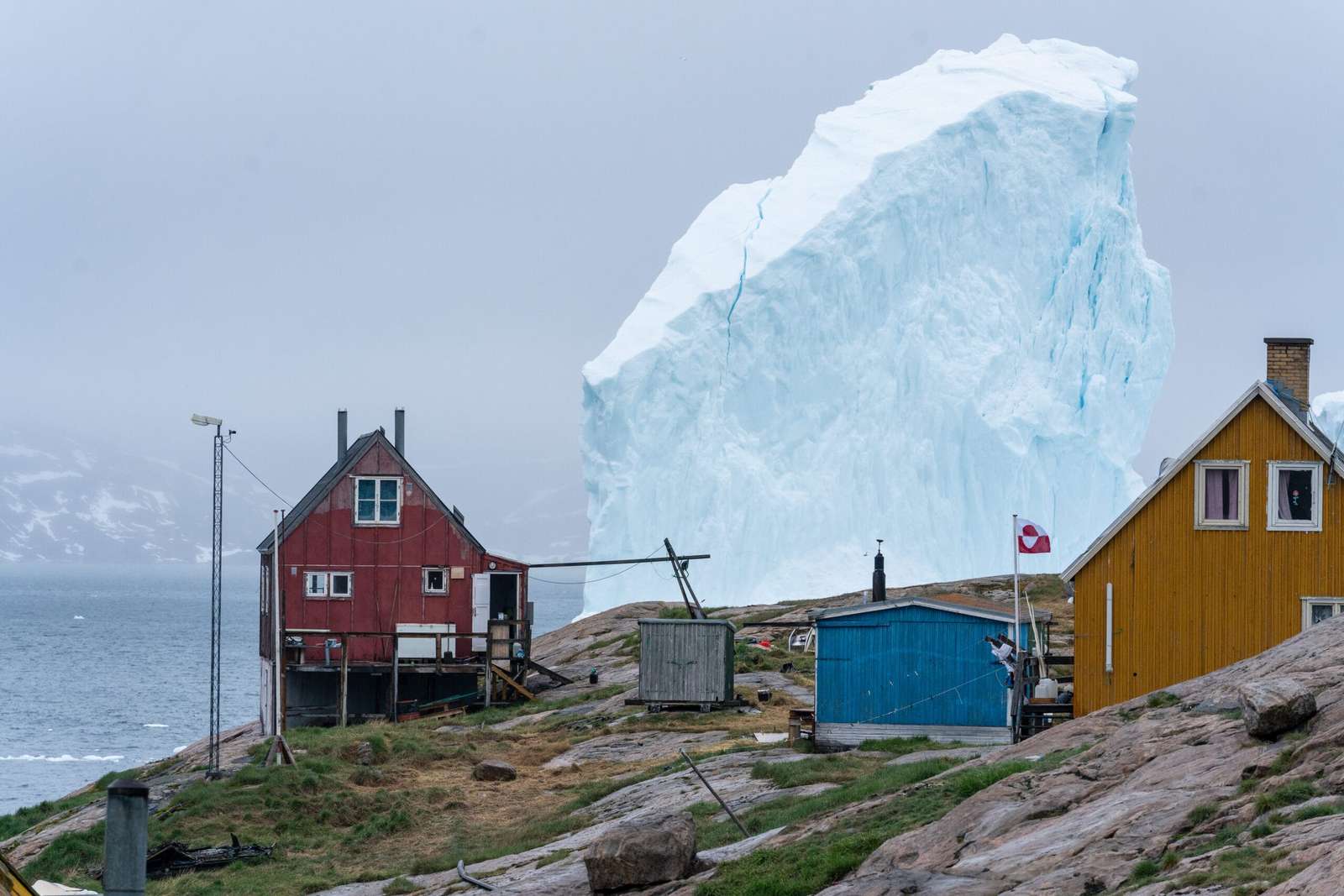 two wooden houses in Greenland with a giant iceberg in the background