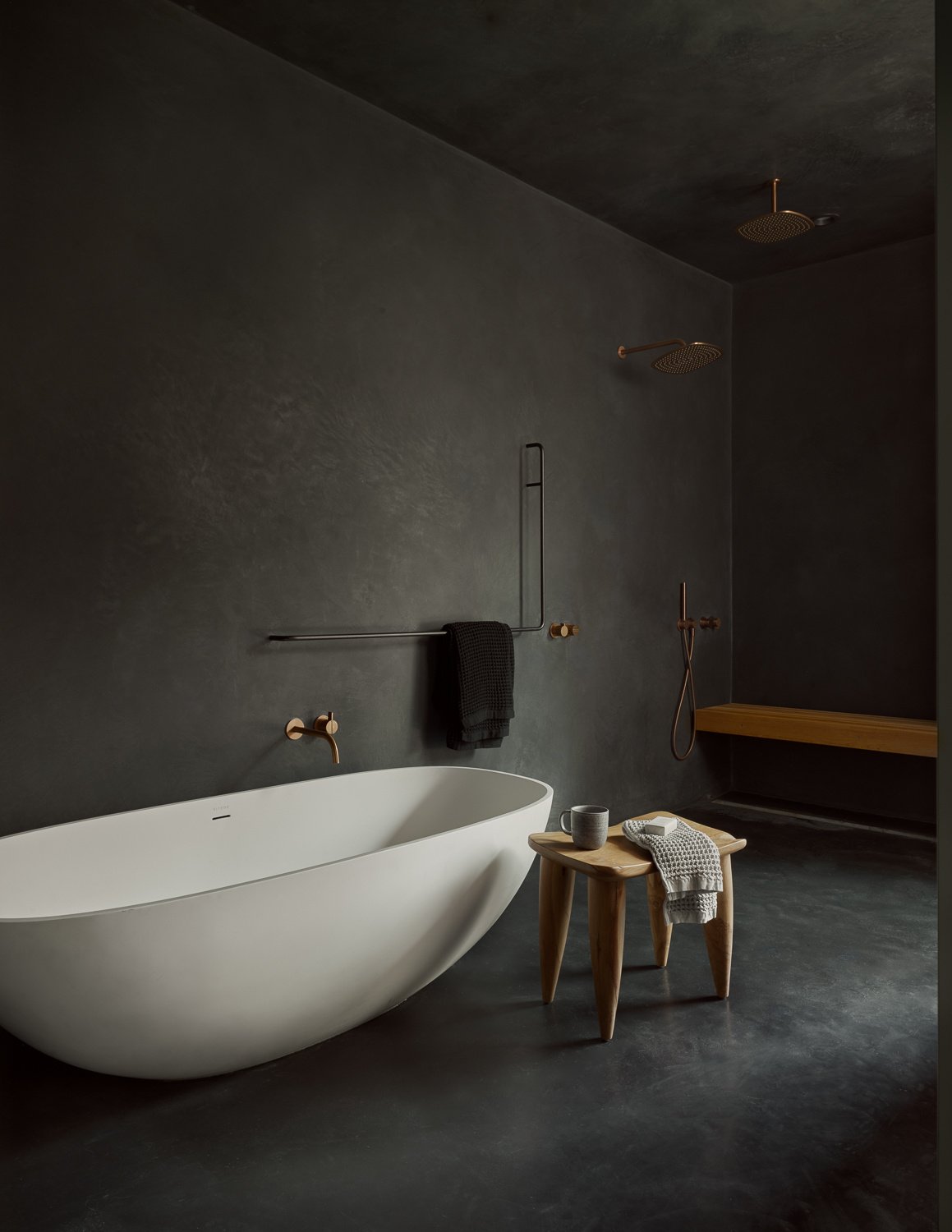The primary bathroom continues the theme of simplicity with purpose. Natural light, thoughtful layout, and a calm, clean aesthetic create a space that feels like a private retreat. A freestanding white bathtub anchors the space, set against dark, textured walls that heighten its minimalist form.