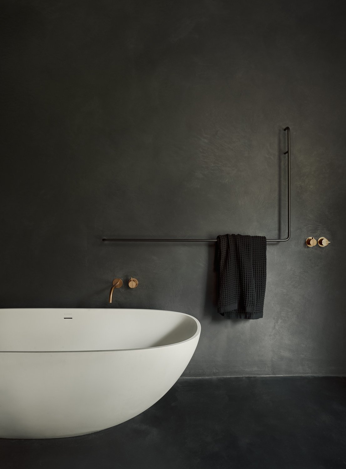 The primary bathroom continues the theme of simplicity with purpose. Natural light, thoughtful layout, and a calm, clean aesthetic create a space that feels like a private retreat. A freestanding white bathtub anchors the space, set against dark, textured walls that heighten its minimalist form.