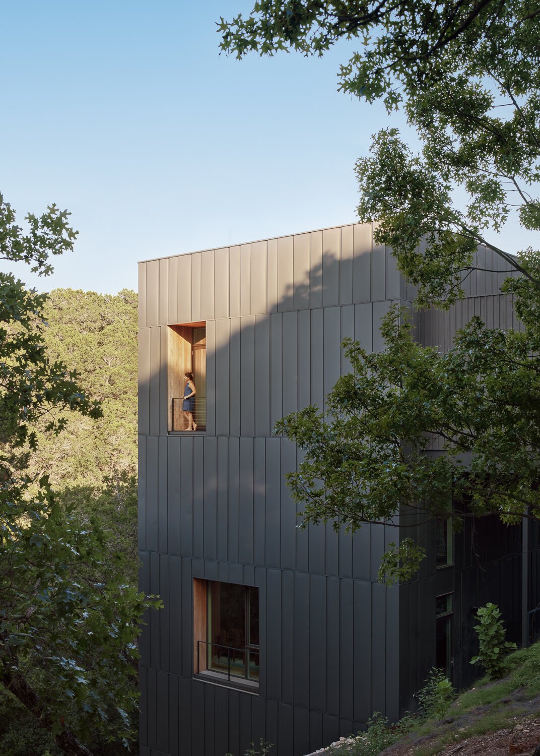 The exterior of this modern home is wrapped in vertical steel panels designed to weather, while deep wood-lined recesses frame curated views and allow light to shift throughout the day.