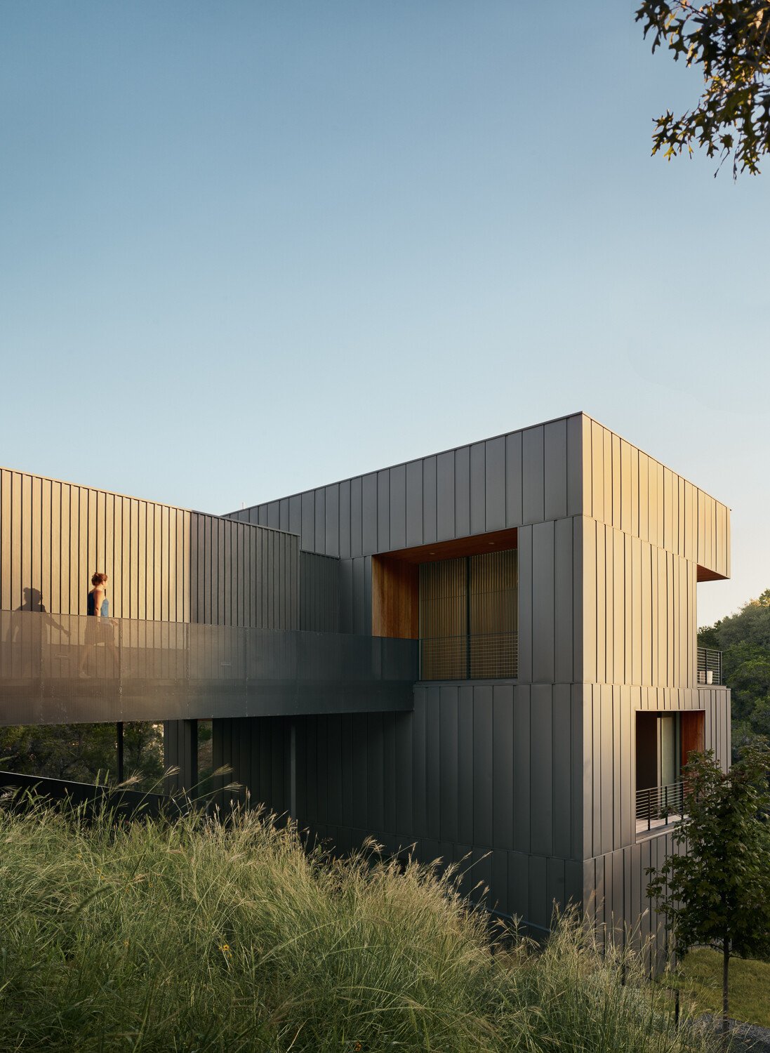 The exterior of this modern home is wrapped in vertical steel panels designed to weather, while deep wood-lined recesses frame curated views and allow light to shift throughout the day.
