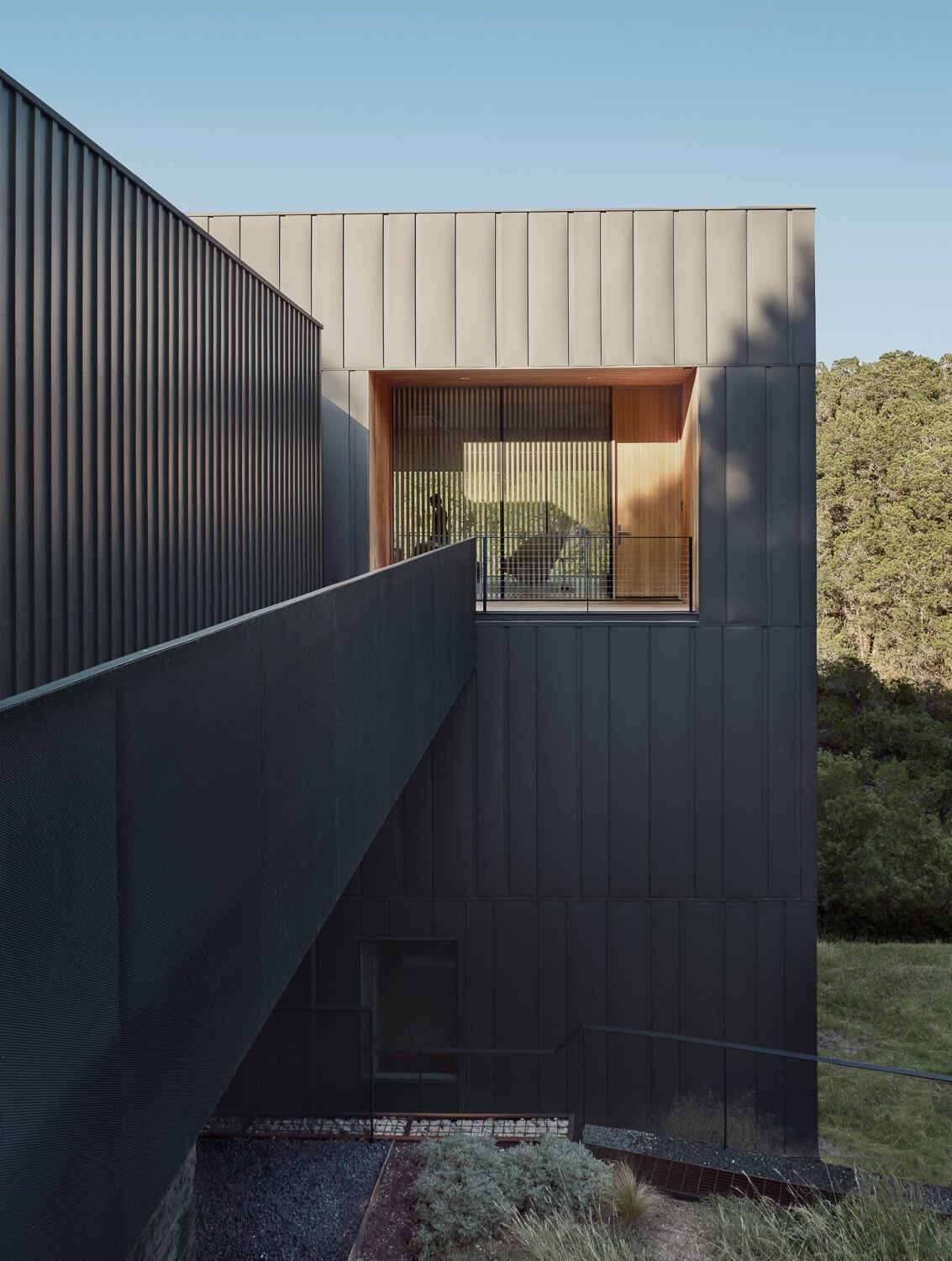 The exterior of this modern home is wrapped in vertical steel panels designed to weather, while deep wood-lined recesses frame curated views and allow light to shift throughout the day.