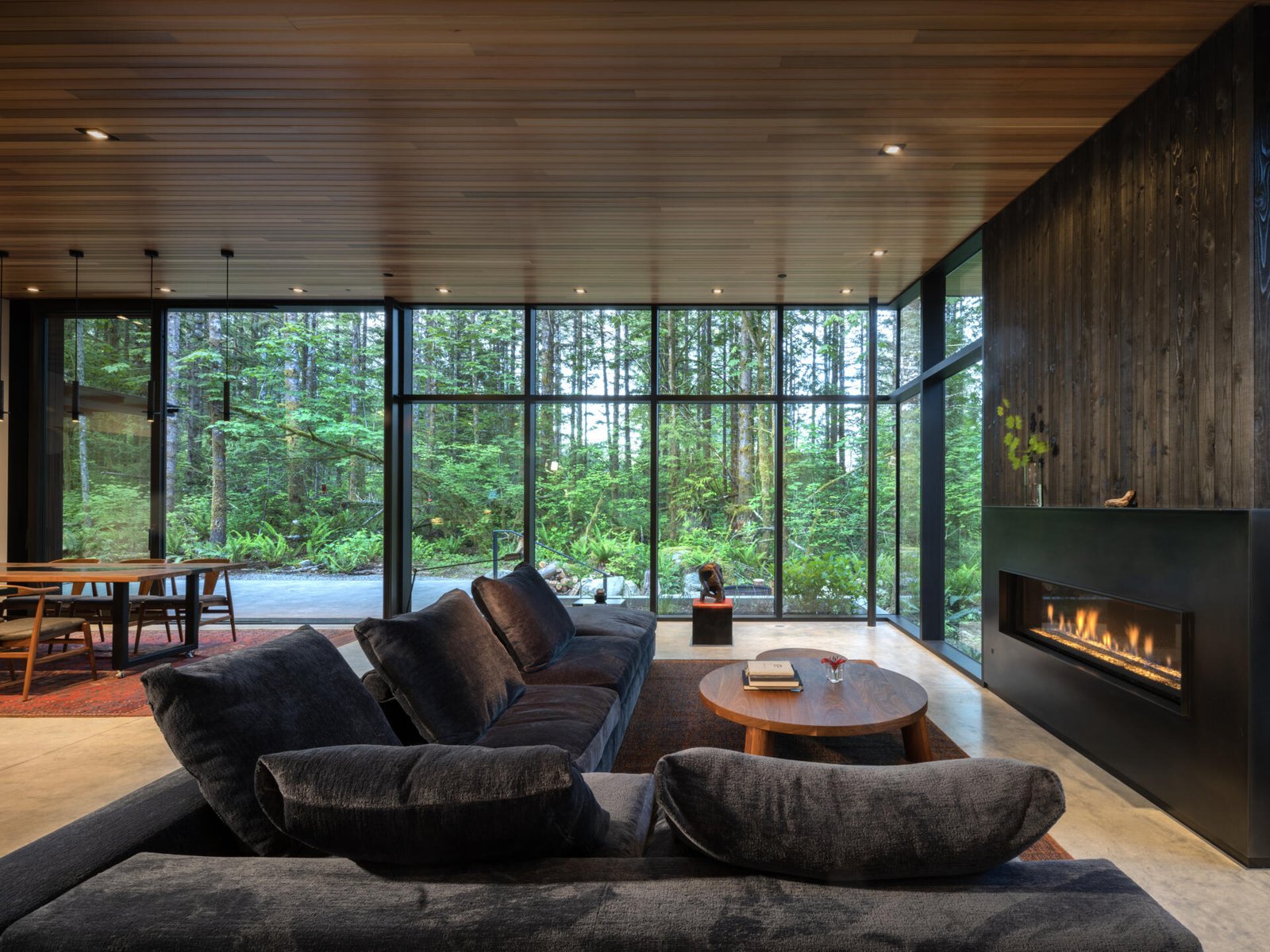 The living room prioritizes views with expanses of windows, and seating oriented toward the fireplace with its steel surround, rather than a screen. Daylight shifts through the space, tracing the sun’s path, bringing softness and warmth to this otherwise rain-heavy region.
