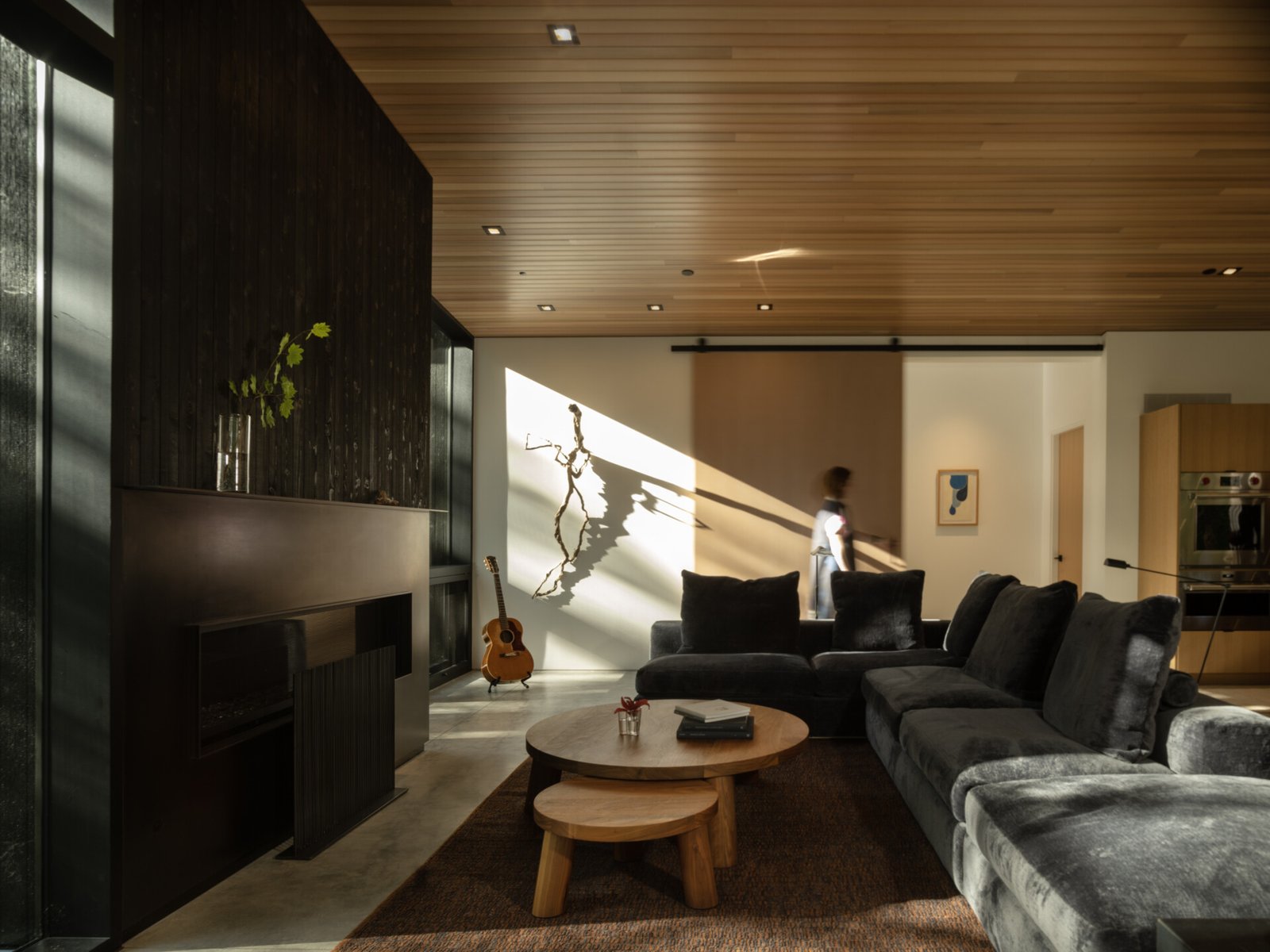 The living room prioritizes views with expanses of windows, and seating oriented toward the fireplace with its steel surround, rather than a screen. Daylight shifts through the space, tracing the sun’s path, bringing softness and warmth to this otherwise rain-heavy region.