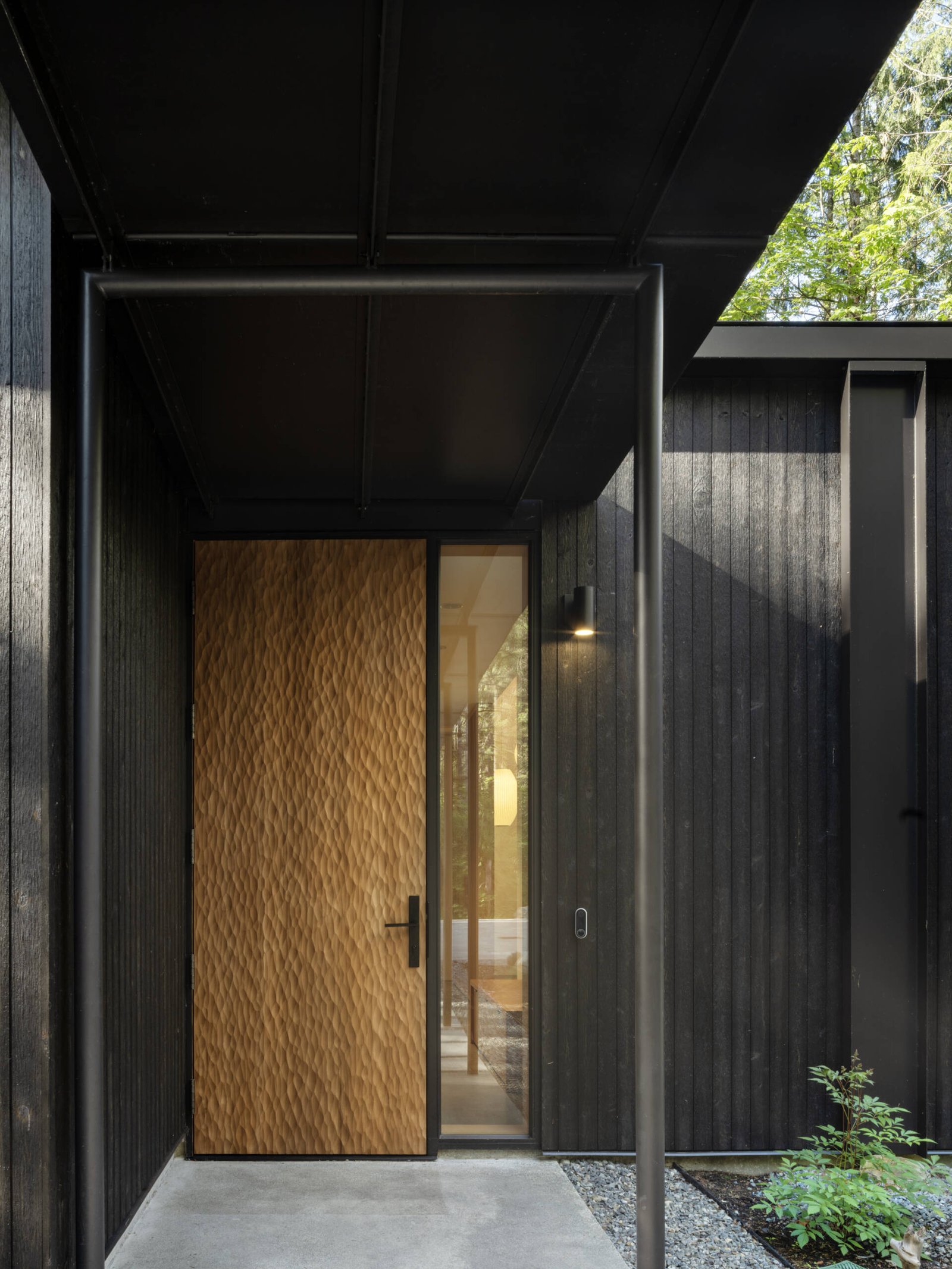 This quiet forest entryway blends wood, stone, and glass to create a seamless transition between outdoors and in.