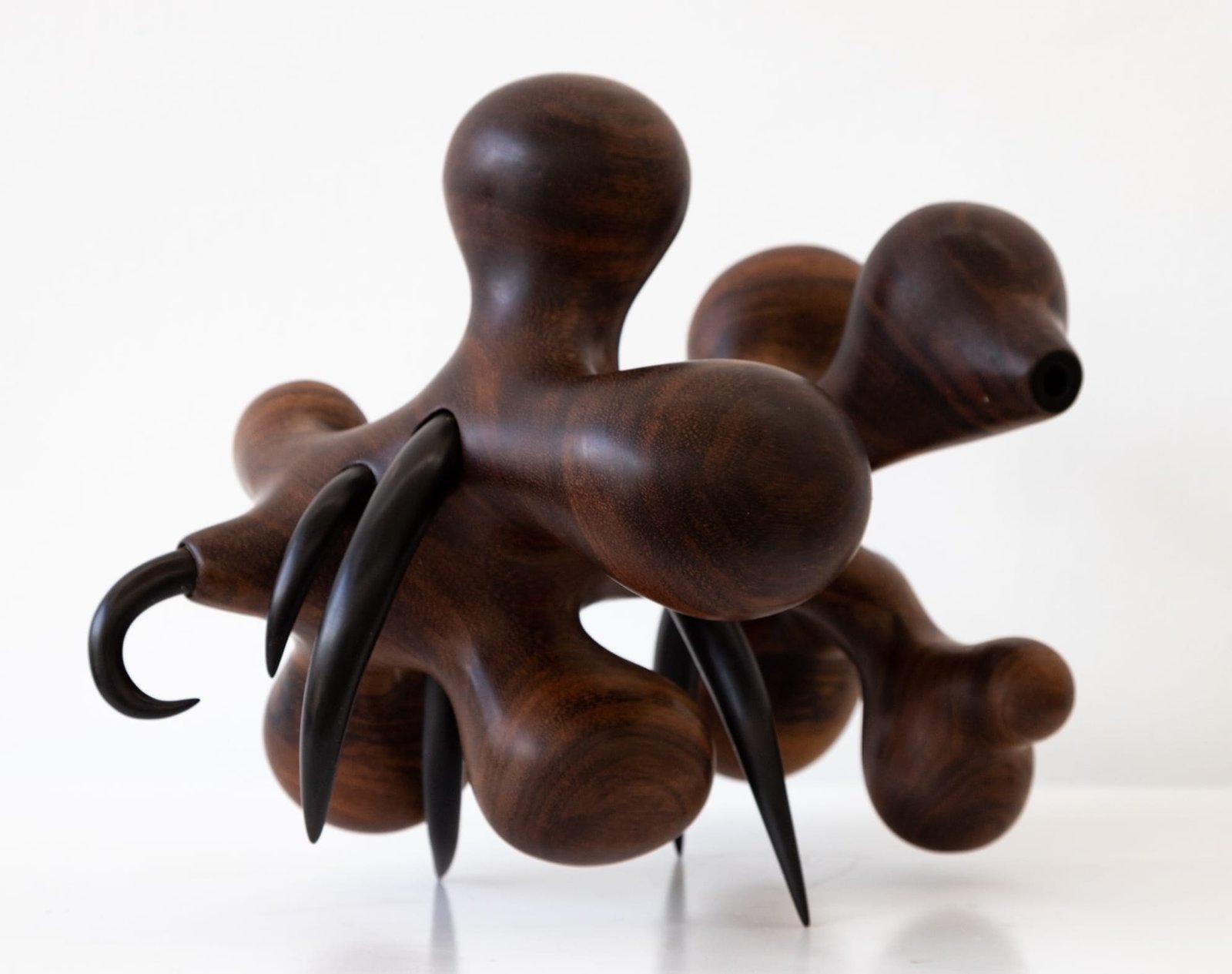 a wooden sculpture by Donald Wasswa with an abstract, sci-fi or sea creature-like form with short, black tentacles