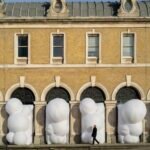 a series of large, white, bulbous, inflatable shapes designed by Steve Messam that stick out of an arched arcade on the first level of a brick building