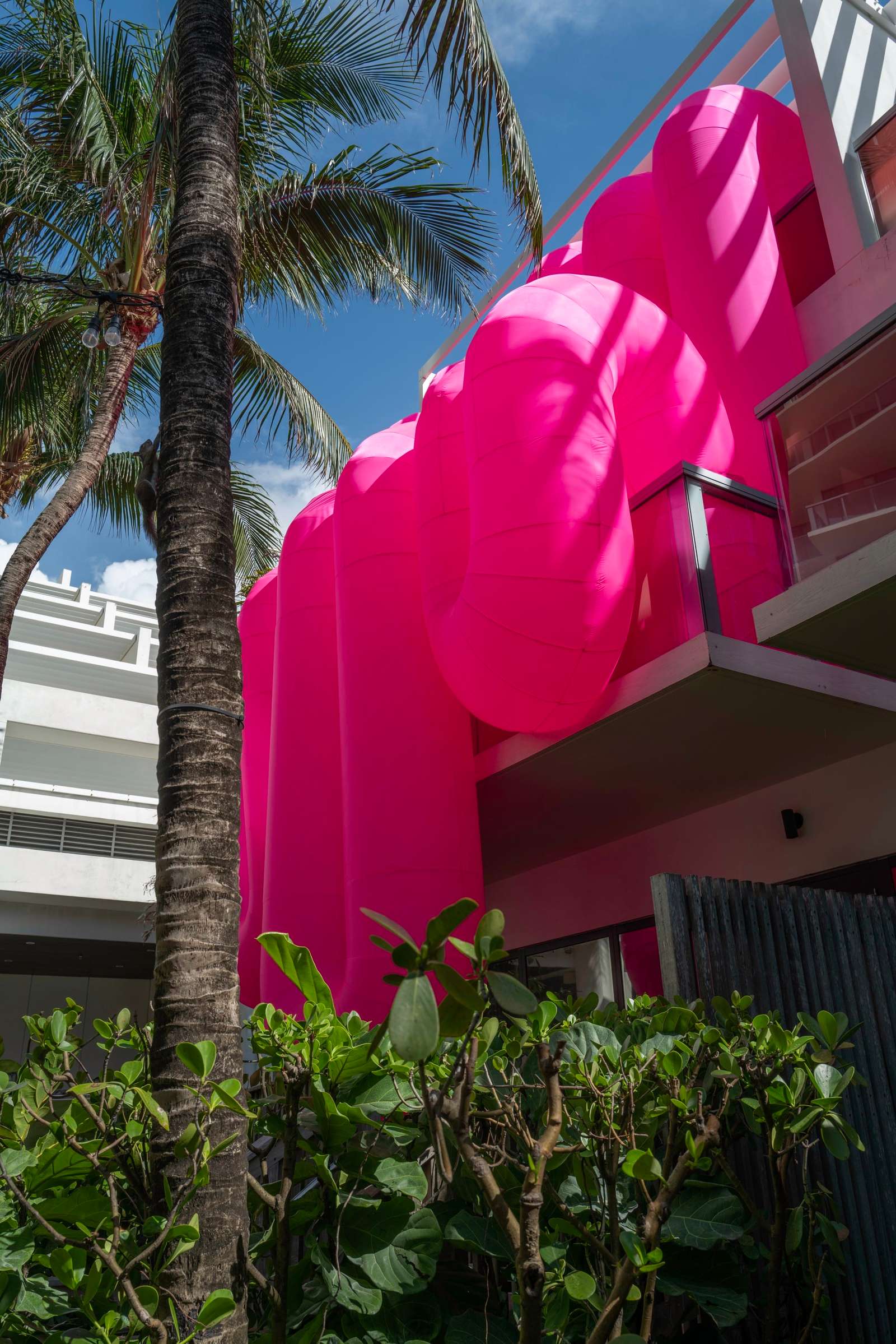 a view looking up at a large-scale inflatable sculpture by Steve Messam of an amorphous, pink form that appears to drape over a balcony