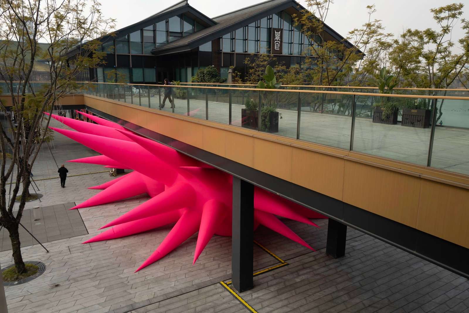 an aerial view of a large-scale inflatable sculpture installation by Steve Messam of two symmetrical, red, spiked forms wedged under a bridge