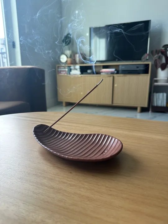 A burning stick of incense above a ridged tray on a coffee table in a living room.