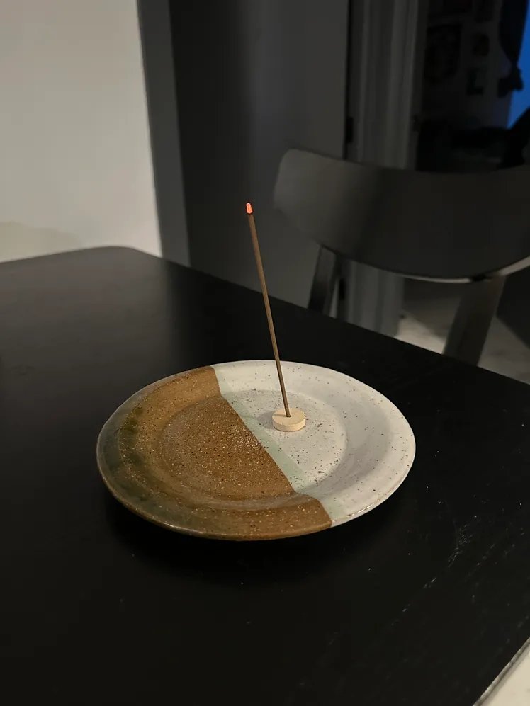Incense stick with a two-tone ceramic plate beneath it.