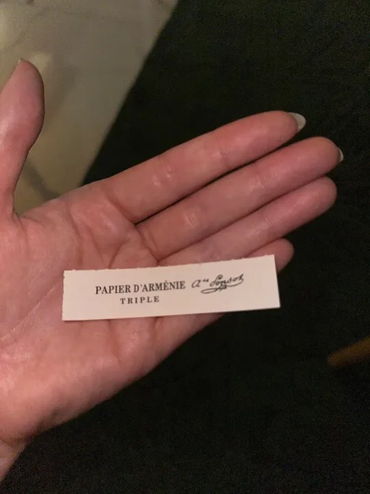 Person's hand holding a small slip of incense paper.