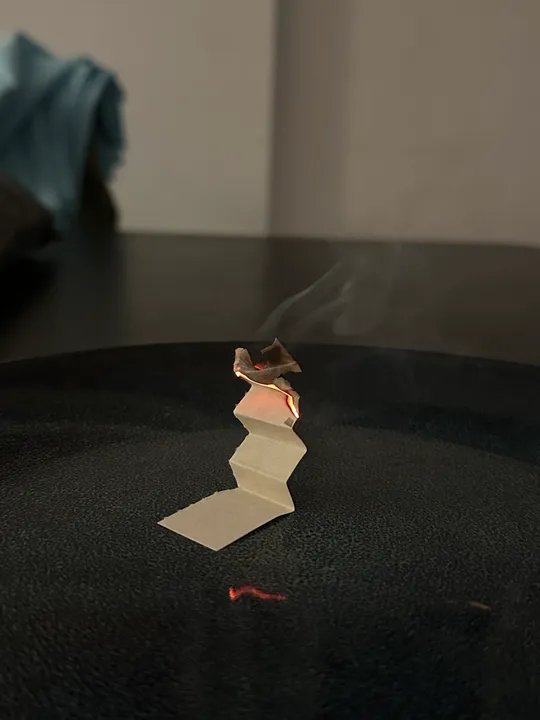 Folded incense paper burning on a plate.