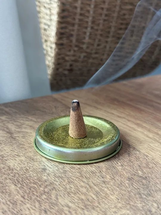 Incense cone burning on a metal lid set on top of a desk.