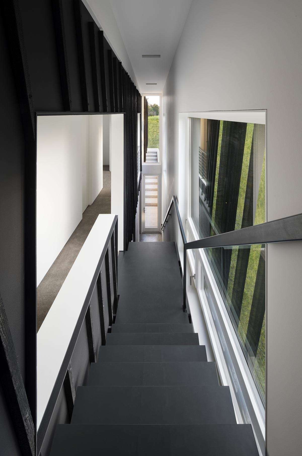 A black sculptural staircase leads to calm, light-filled bedrooms where Shou Sugi Ban details continue the home’s cohesive design.