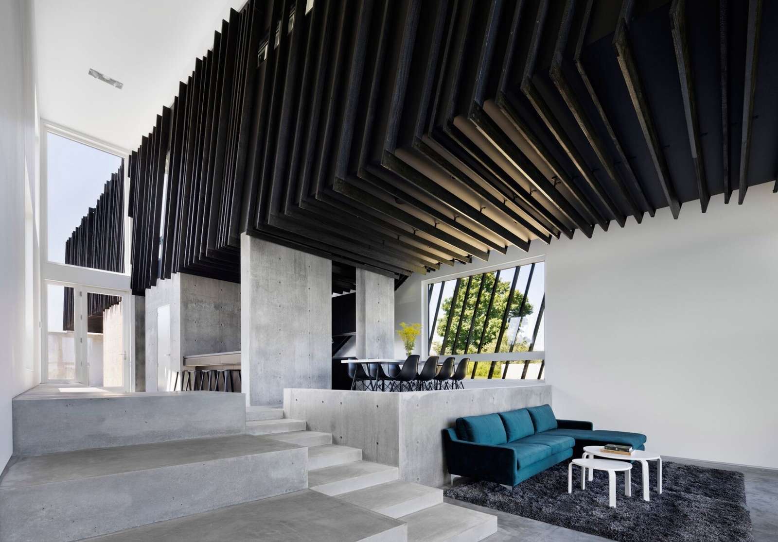 A bright blue couch and panoramic mountain views bring life and warmth to this minimalist living room framed by concrete and glass.