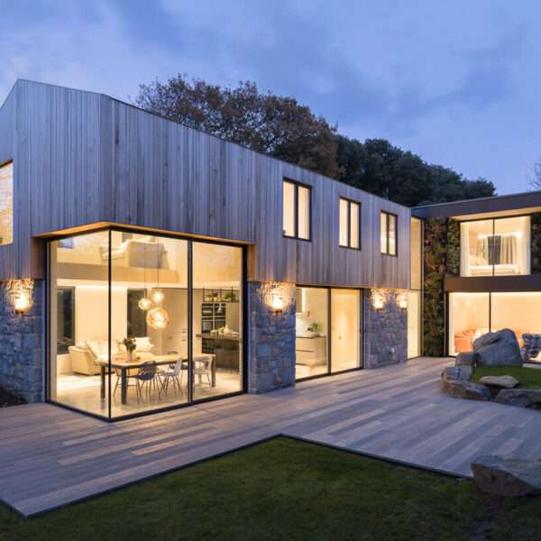 This modern home is wrapped in Guernsey granite, cedar cladding, and a living wall with 13 native species that soften the structure and blend it into the forested setting.
