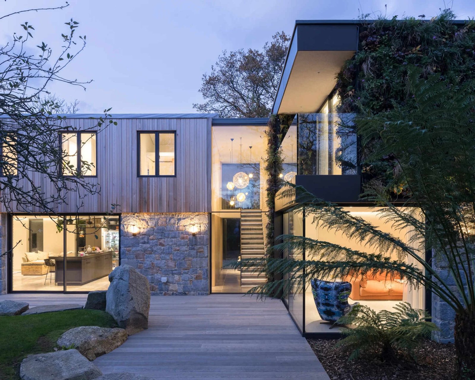 This modern home is wrapped in Guernsey granite, cedar cladding, and a living wall with 13 native species that soften the structure and blend it into the forested setting.