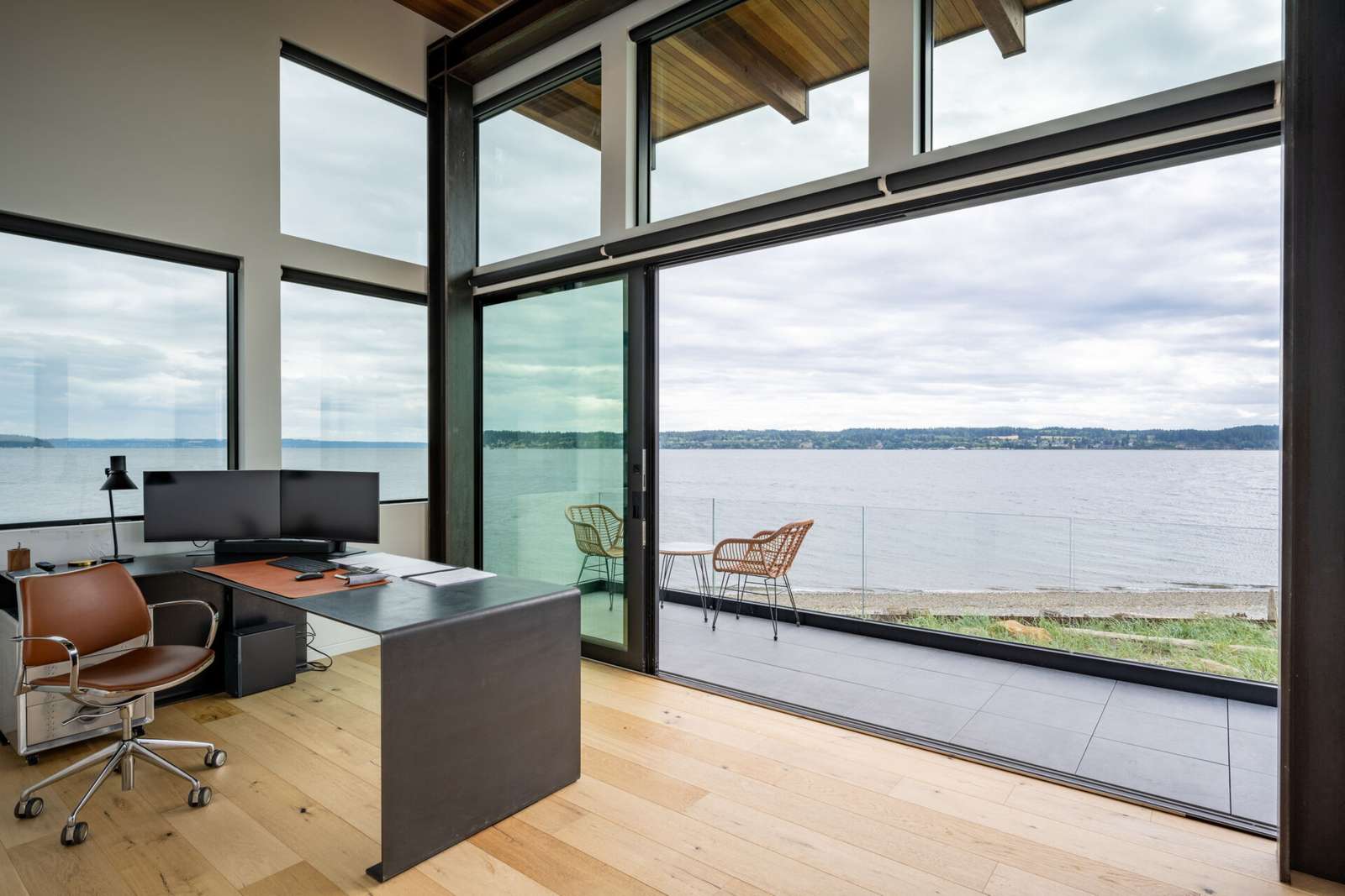 A modern home office opens to a balcony with glass railing, providing uninterrupted views.
