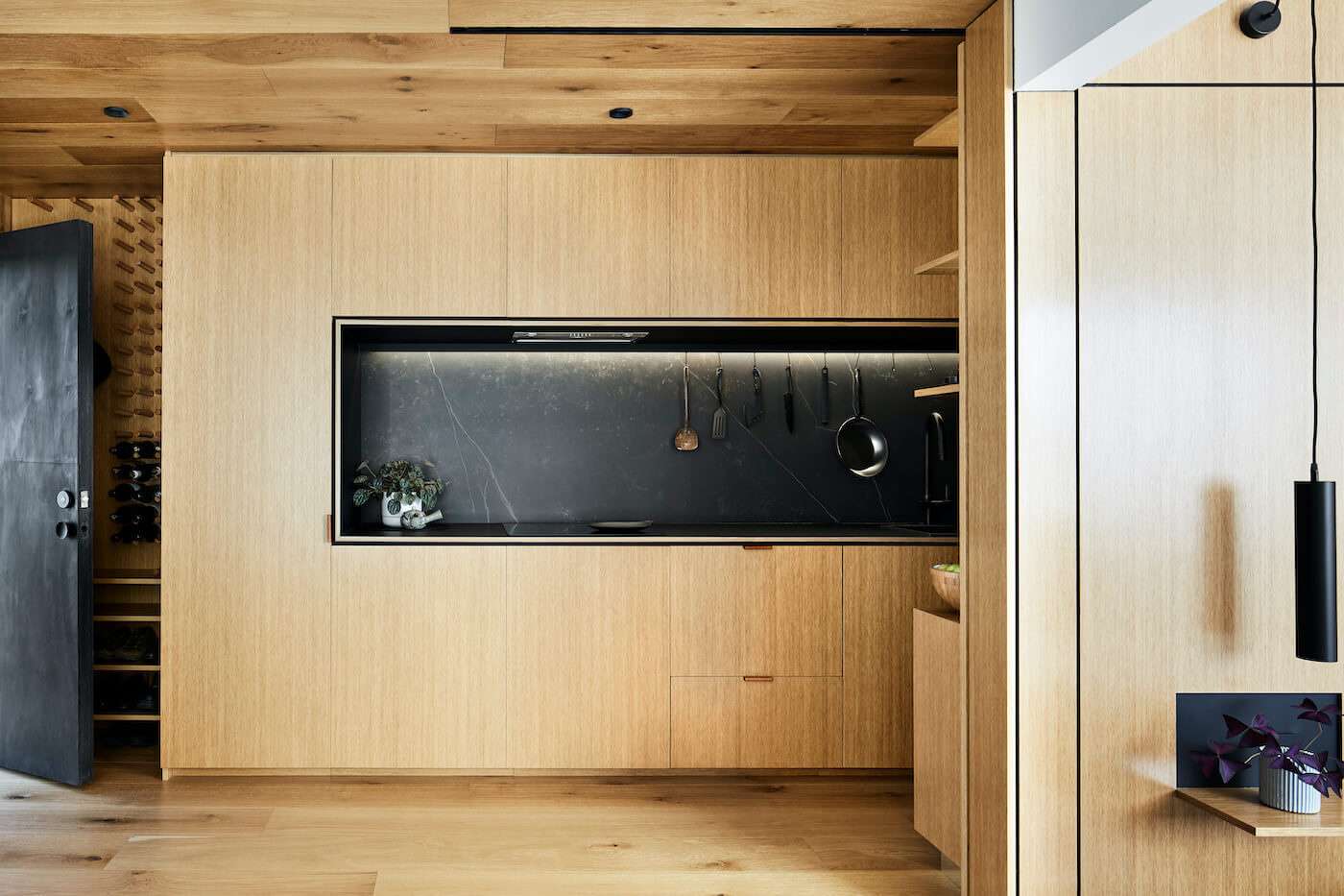 A long timber kitchen with black accents hides appliances and maximises bench space inside this compact Melbourne apartment.