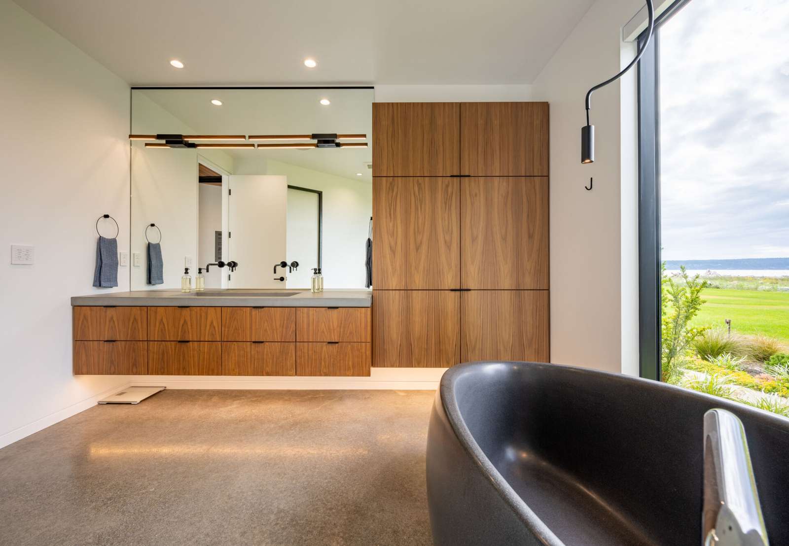 The primary bathroom includes a floating wood vanity with a freestanding sculptural black bathtub, and an eye-catching shower.