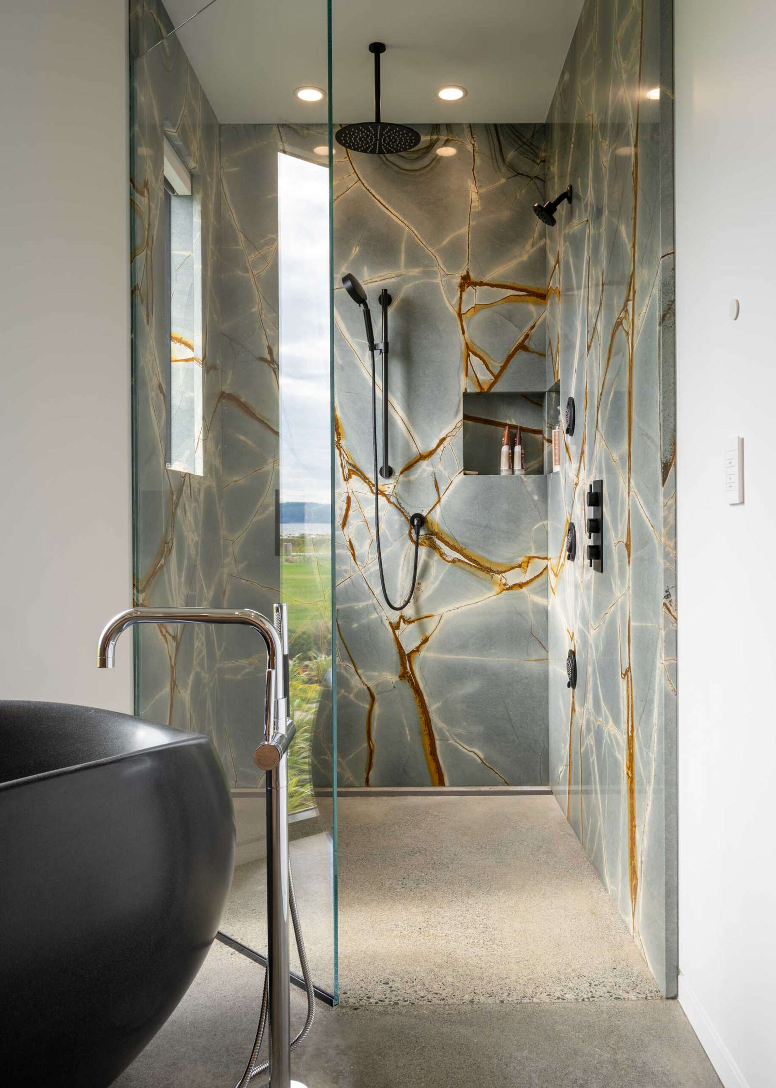 The primary bathroom includes a floating wood vanity with a freestanding sculptural black bathtub, and an eye-catching shower.