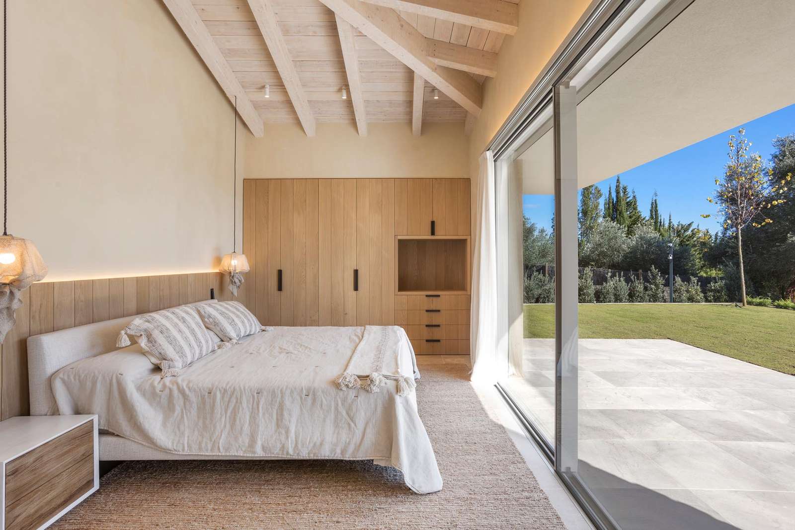 A modern bedroom with wood accents, pendant lights, and a large sliding glass door that opens to a patio.